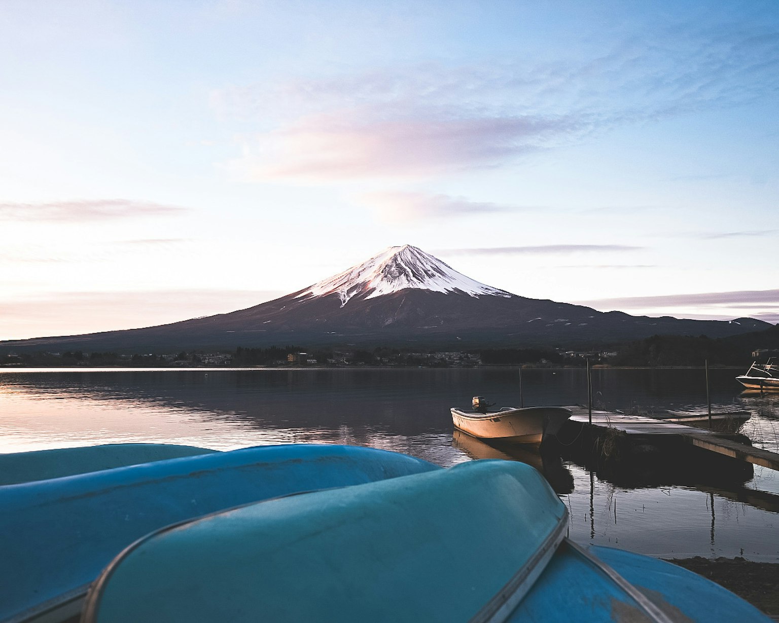 富士山的风景与宁静的湖泊前景中的蓝色船只和黎明的天空