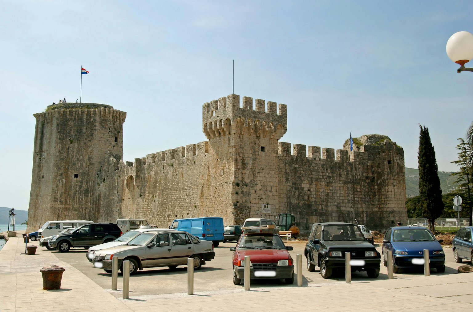 Château médiéval avec murs en pierre et voitures garées