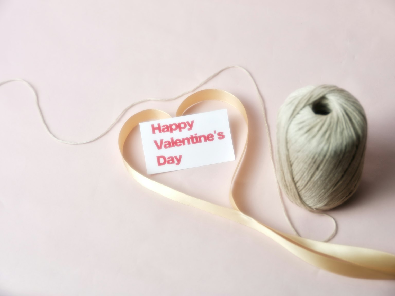 Heart-shaped ribbon with a card saying Happy Valentine’s Day next to a spool of twine