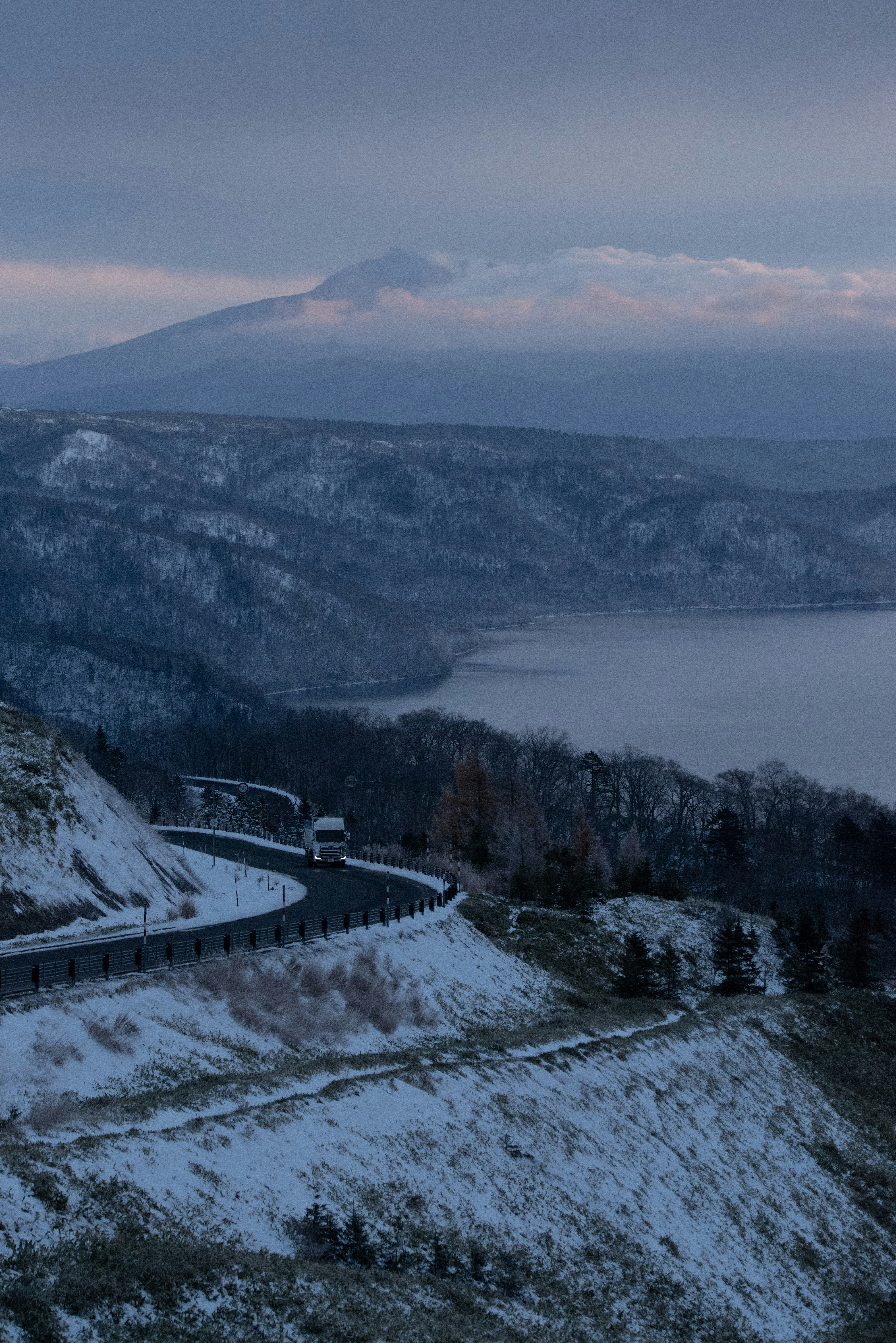 雪の残る丘陵と湖を望む山並みの景色
