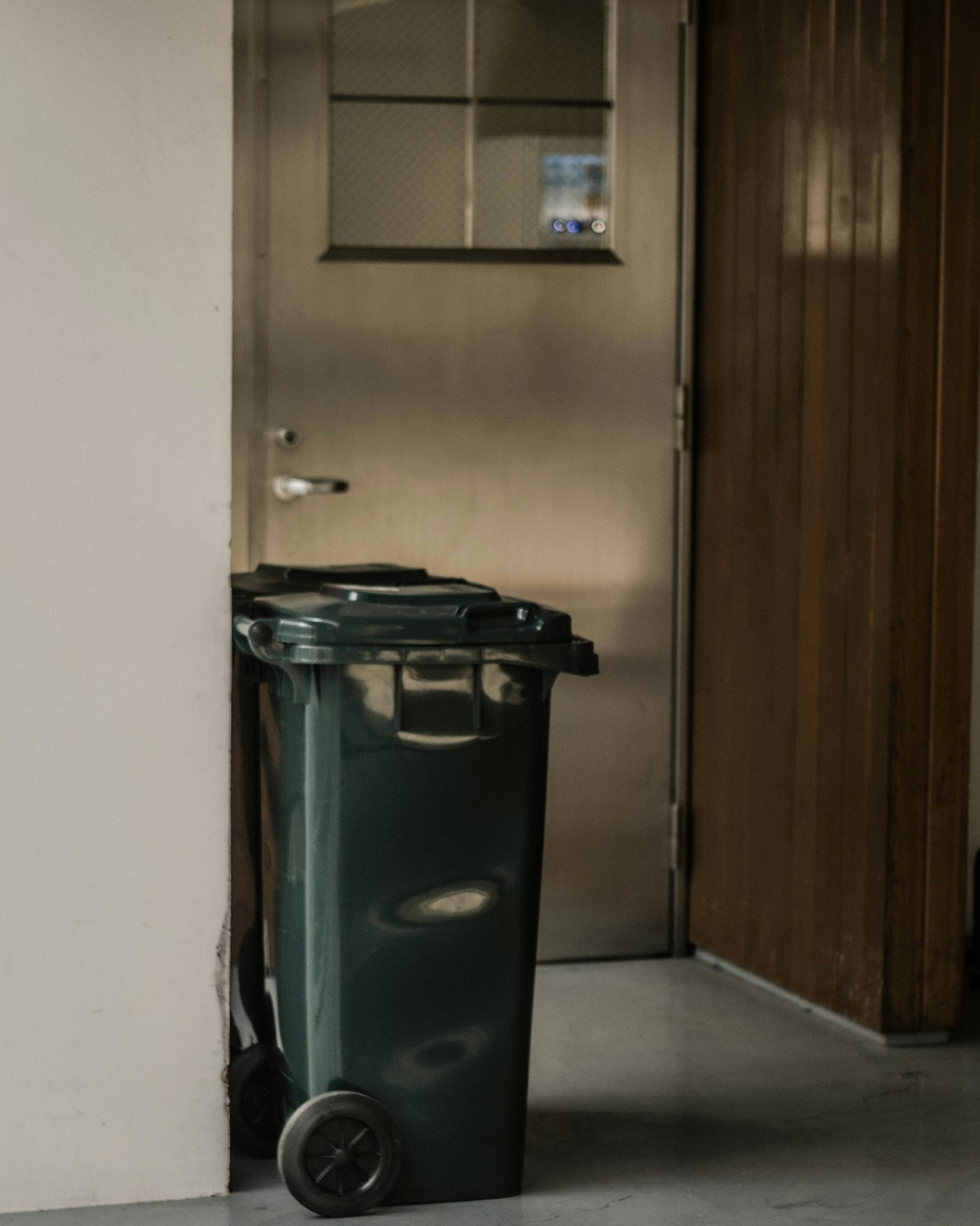 Un bidone della spazzatura verde posizionato vicino a una porta in un ambiente interno