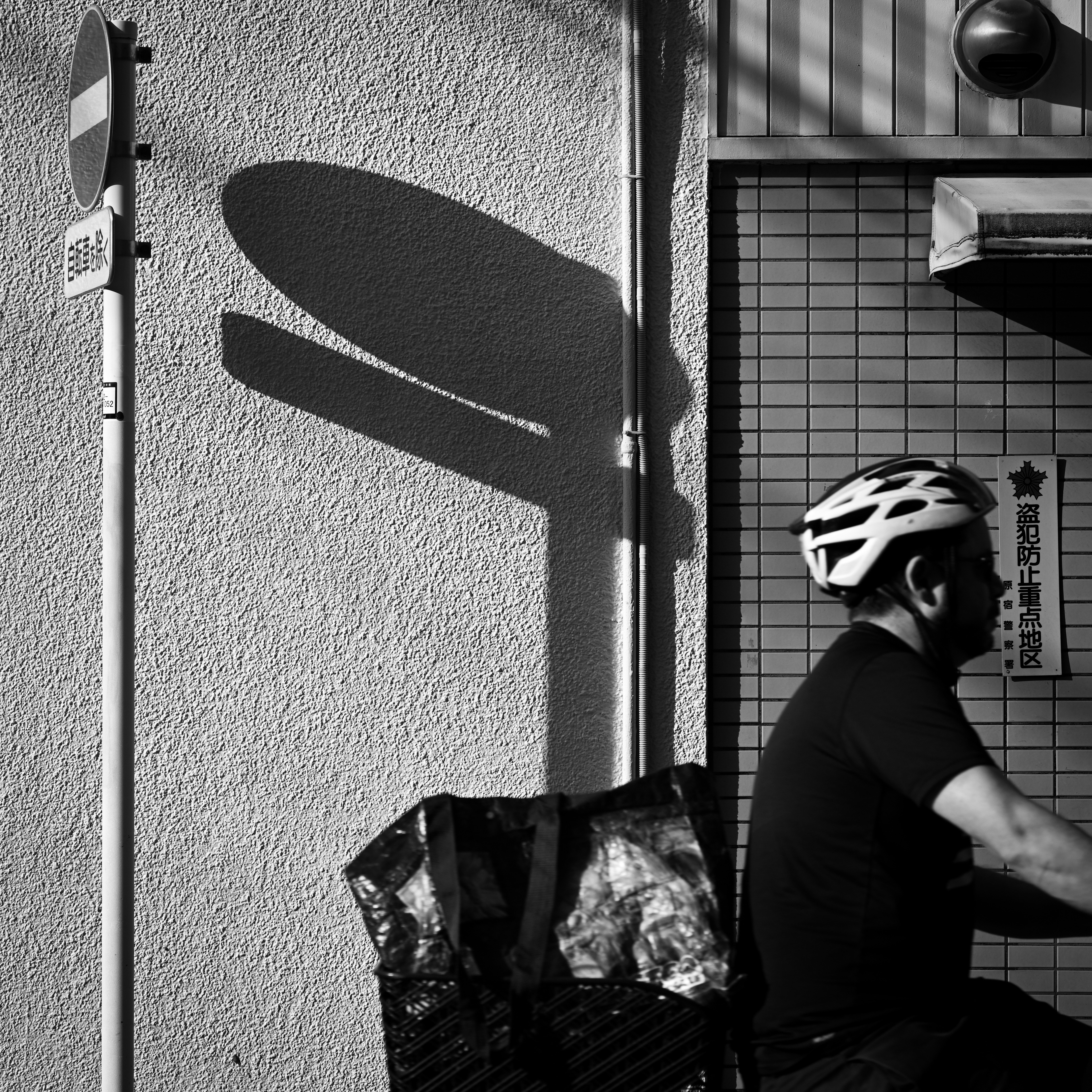 斜光のある東京の路地で自転車ヘルメットと影が交差する標識前の風景