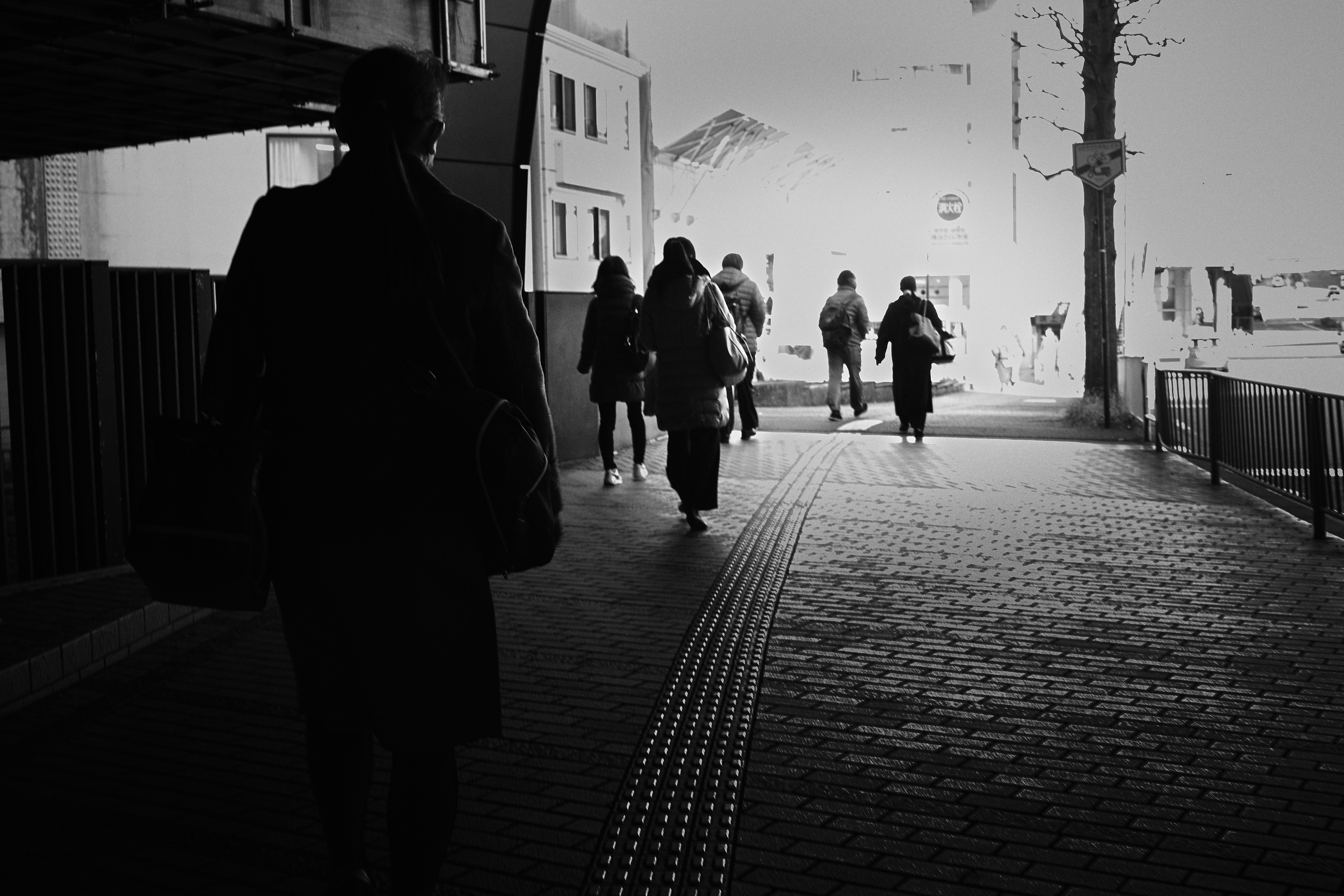 Black and white street scene with people walking on a concrete sidewalk