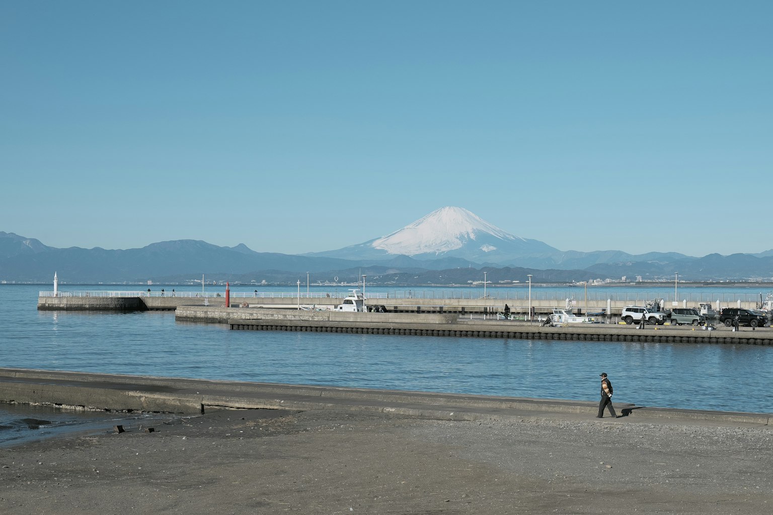 一個人在海灘上散步，背景是平靜的海洋和山脈