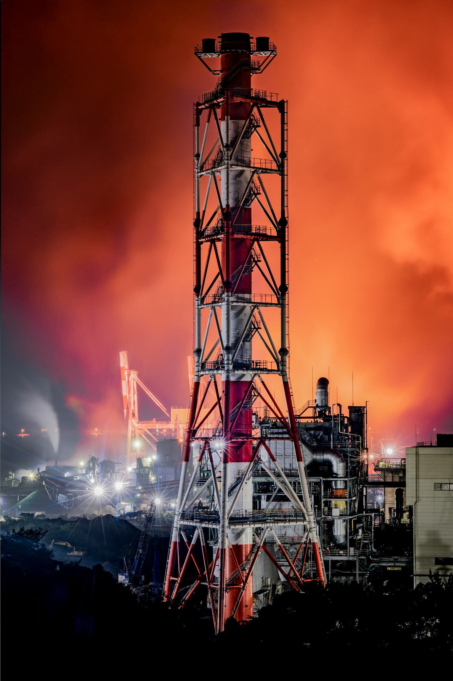 Cheminée rouge et blanche devant un paysage industriel avec un ciel orange