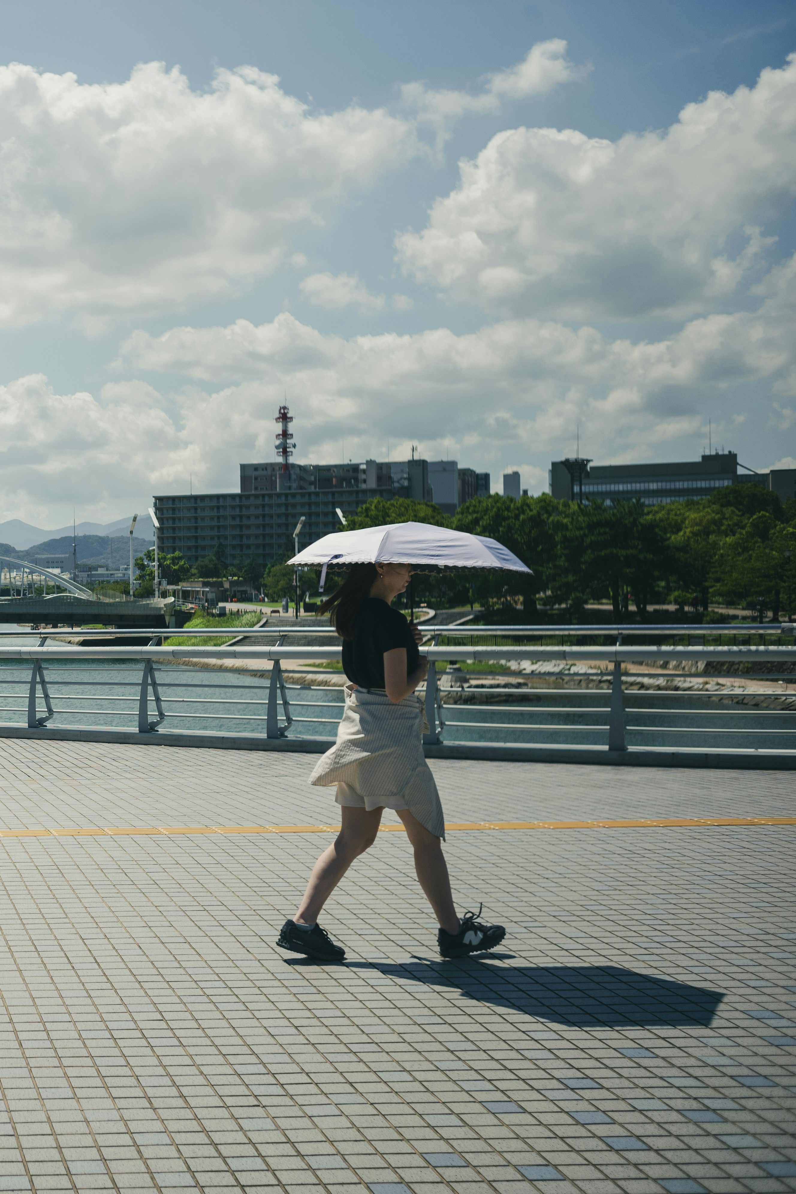 Une personne marche sur une promenade au bord de la rivière à Kokura sous un ciel bleu