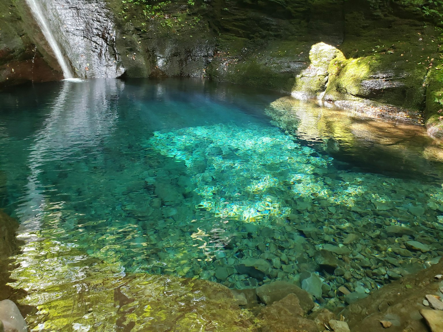 Klares blaues Teich mit Wasserfall und steiniger Umgebung