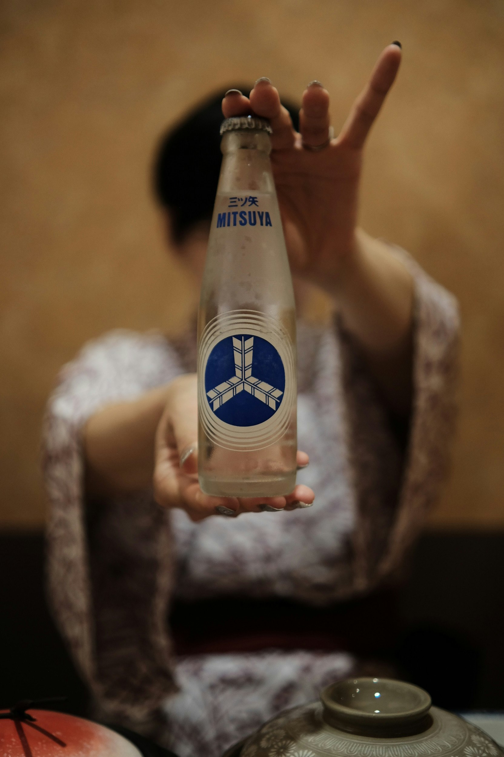 手に持つ「MITSUYA」サイダーのボトルと飲み物のある室内シーン