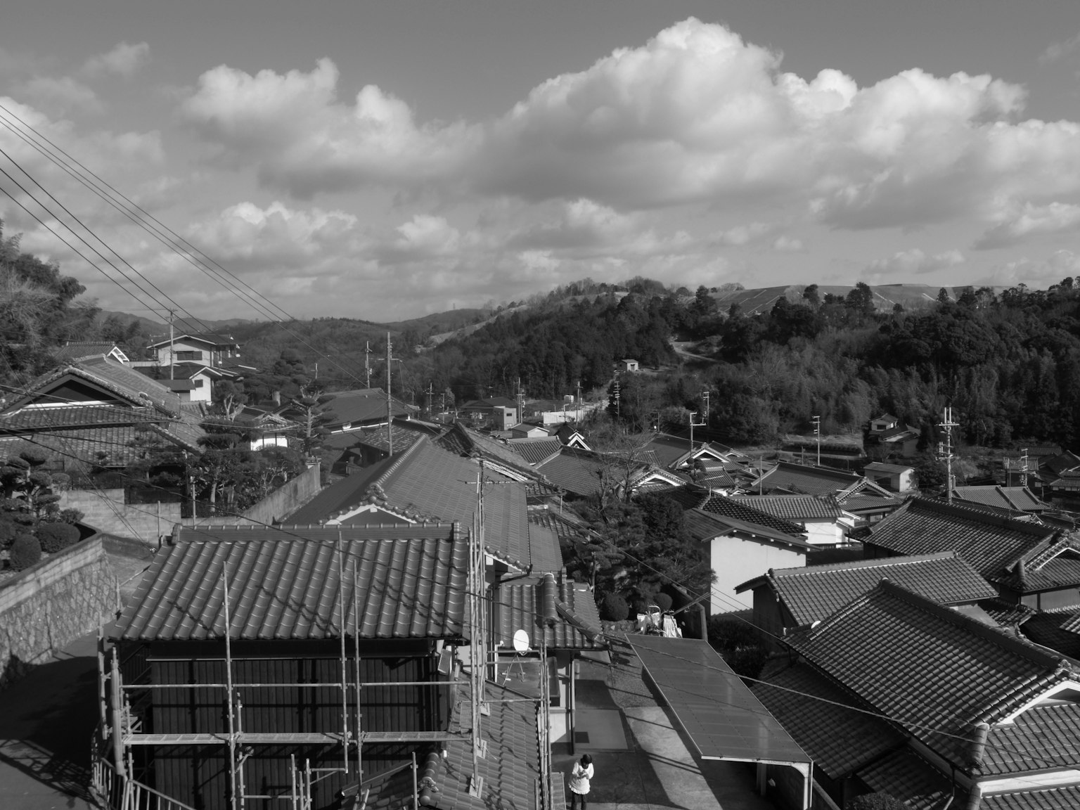 Black and white landscape photo showing town view from rooftop with cloudy sky and green hills