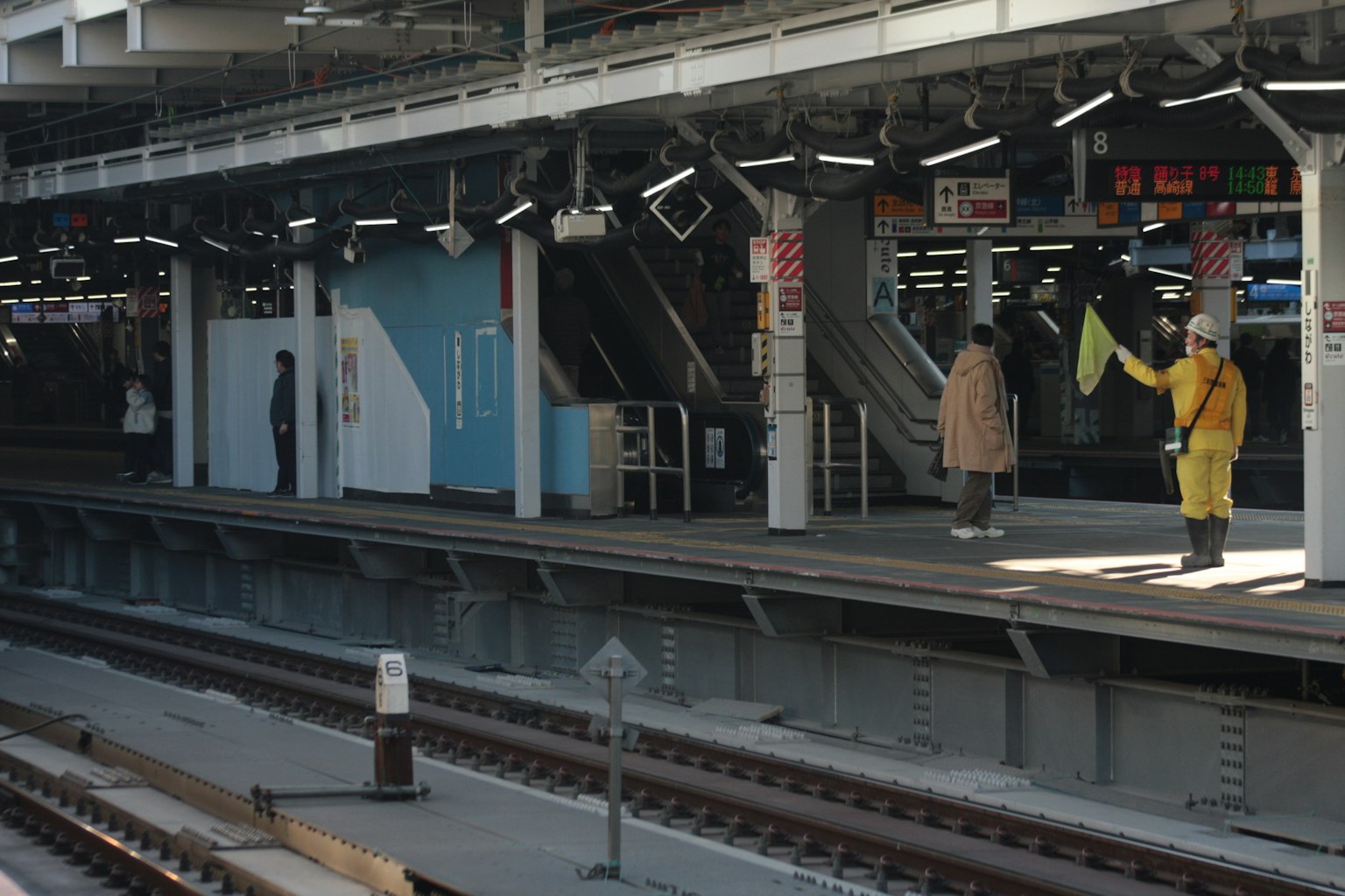 Plateforme d'une gare avec un travailleur tenant un drapeau jaune et des passagers