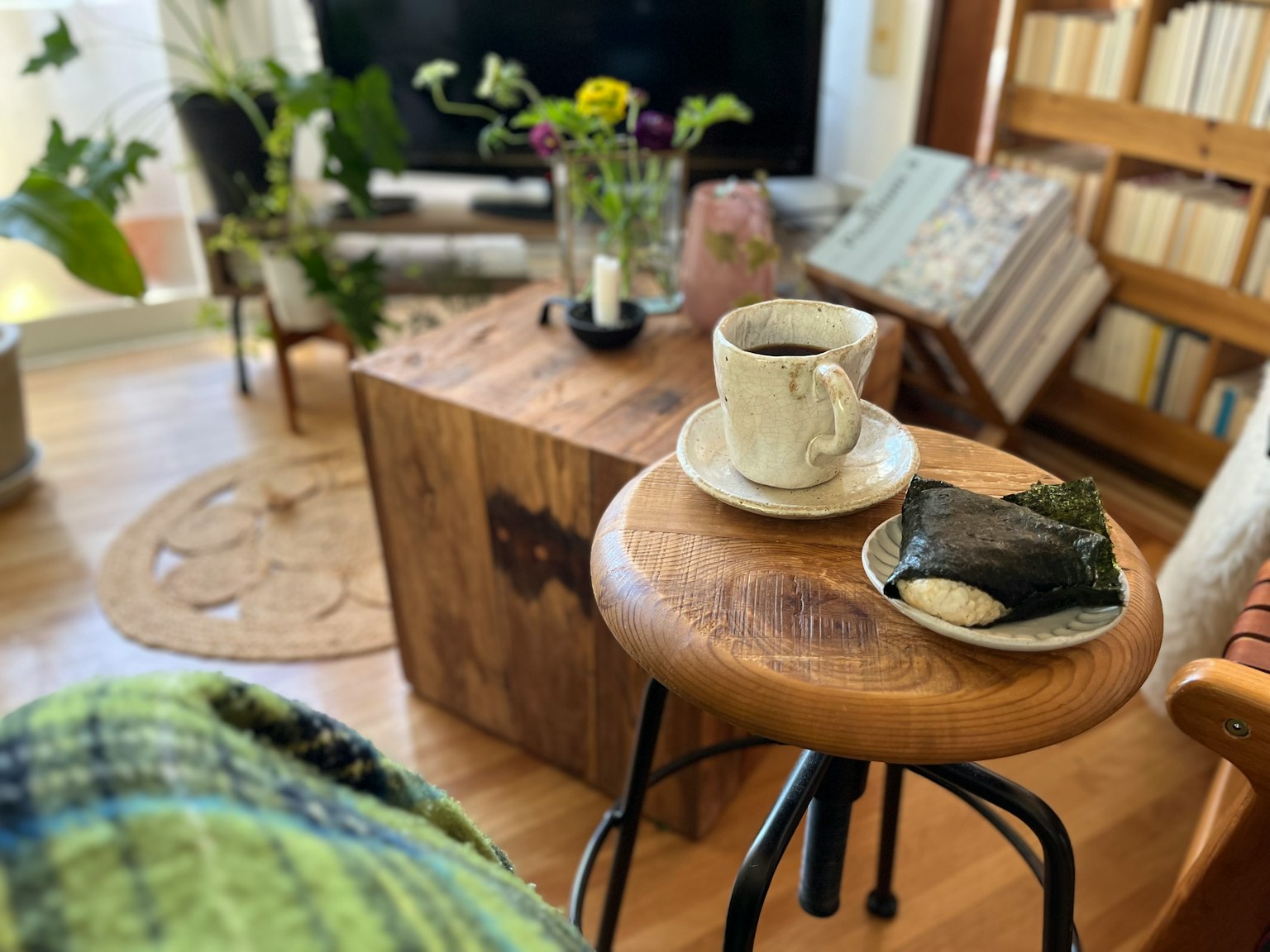 Salon confortable avec une table en bois et un tabouret recouvert d'une couverture verte contenant une tasse de café et un rouleau de sushi