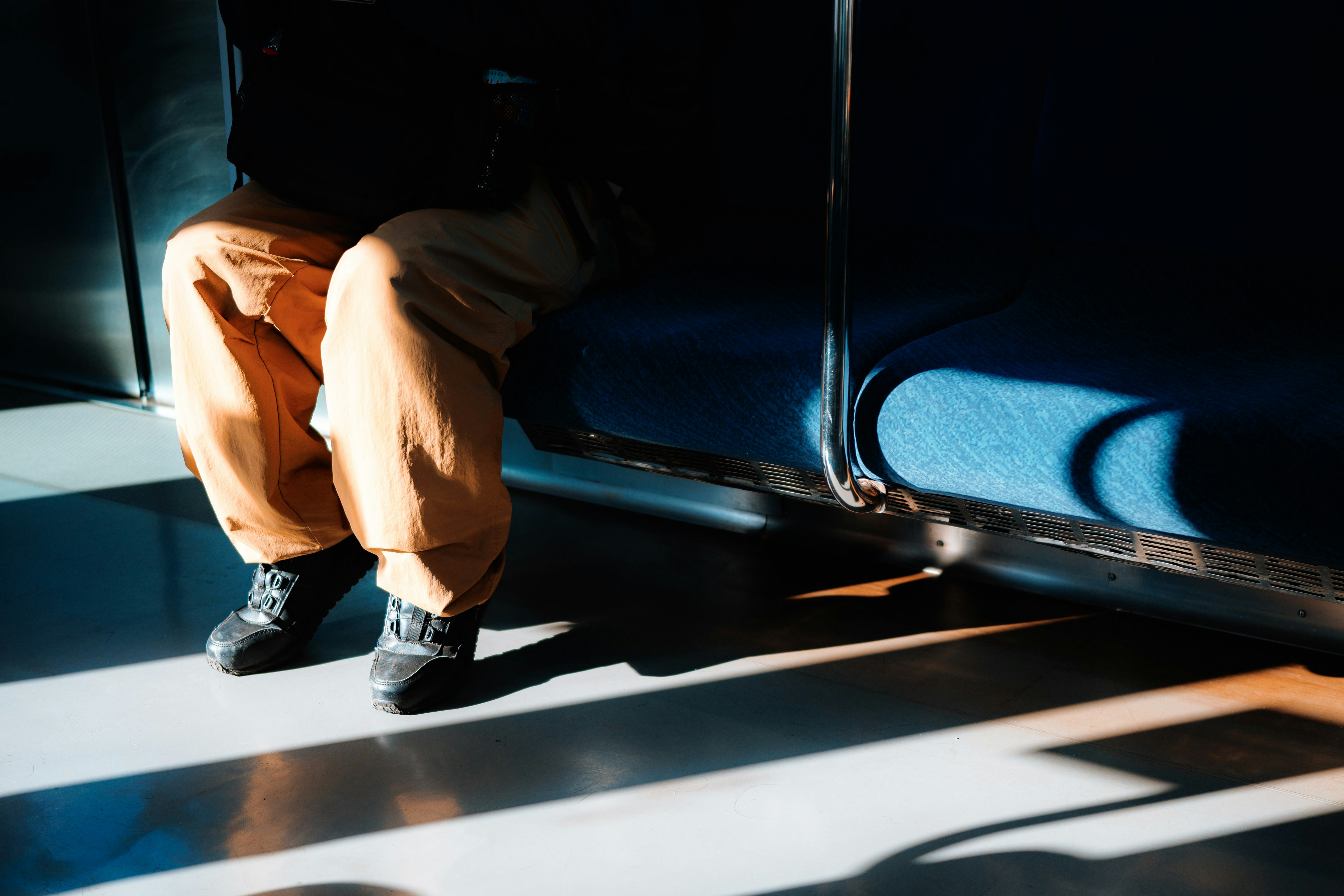電車の中で座っている人の足元の写真 明るい光と影が交差する