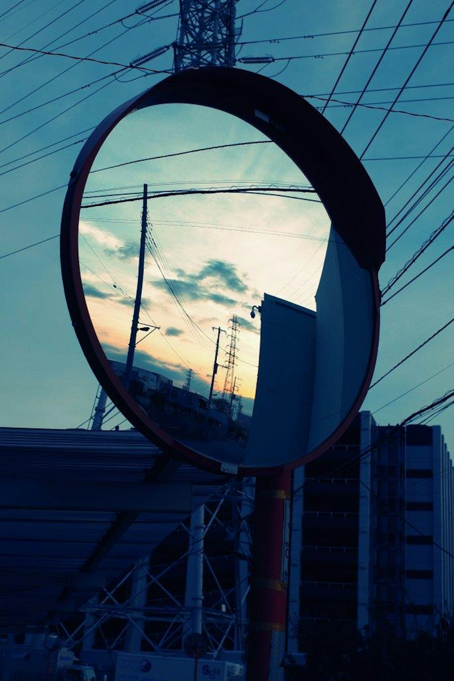 Riflesso del tramonto e dei cavi elettrici in uno specchio stradale