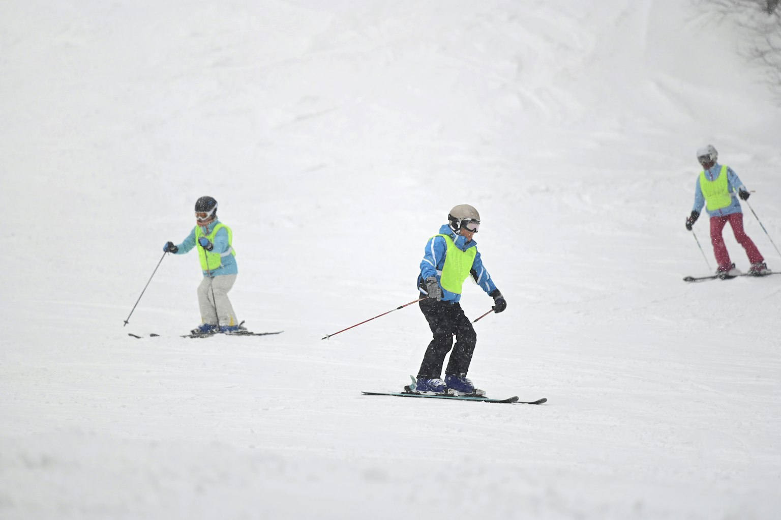 Tiga pemain ski di lereng bersalju mengenakan rompi kuning cerah