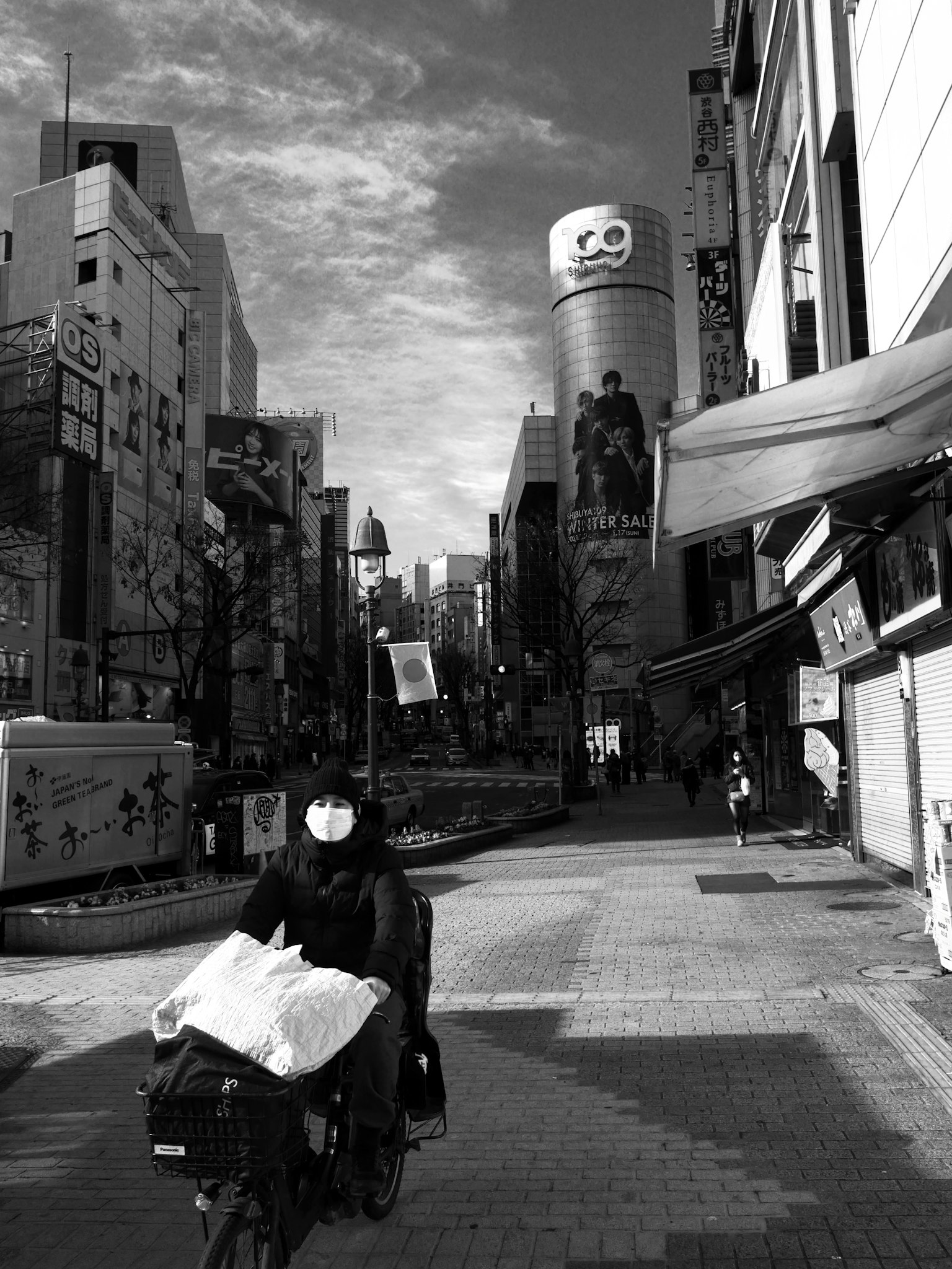 Black and white street scene featuring a delivery person on a bike with tall buildings in the background