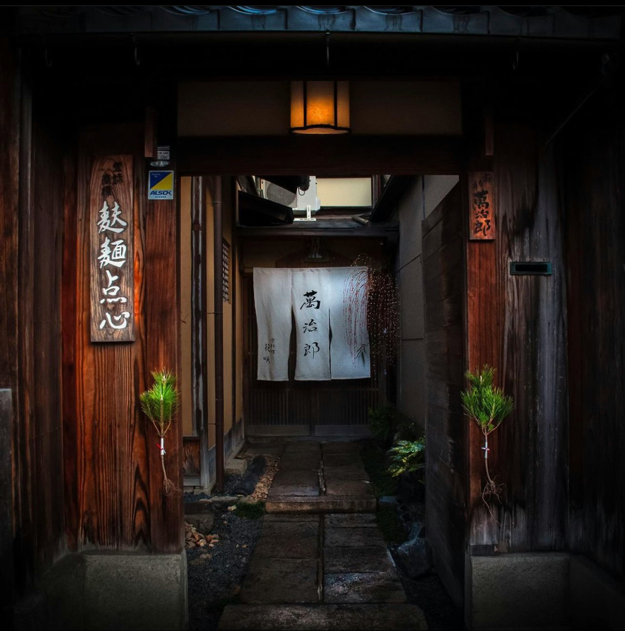 narrow alley with wooden storefronts, hanging noren and lantern light