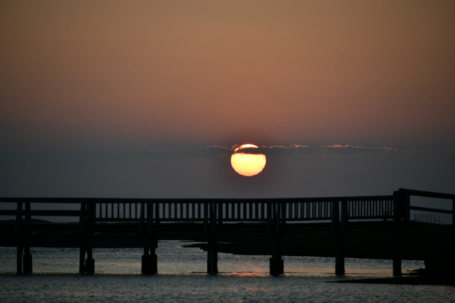 Puesta de sol sobre el mar con un muelle de madera