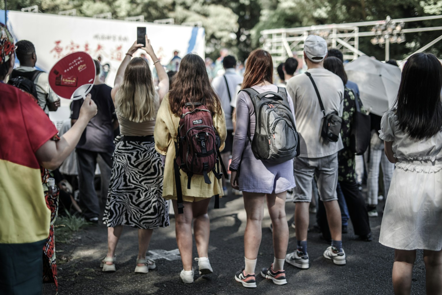 Audience watching an event with people from behind colorful outfits and backpacks
