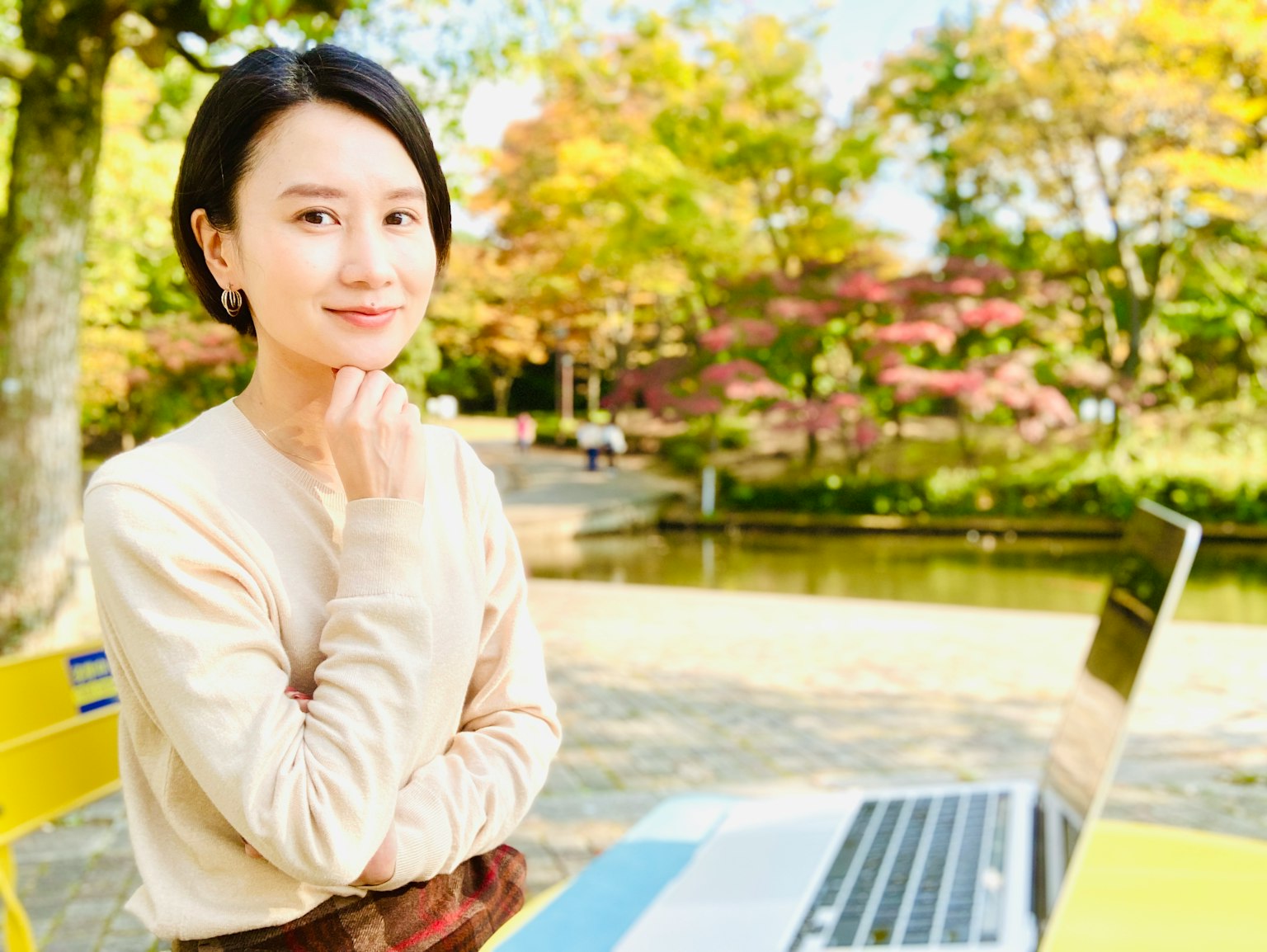 Eine Frau, die in einem Park umgeben von herbstlichem Laub einen Laptop benutzt