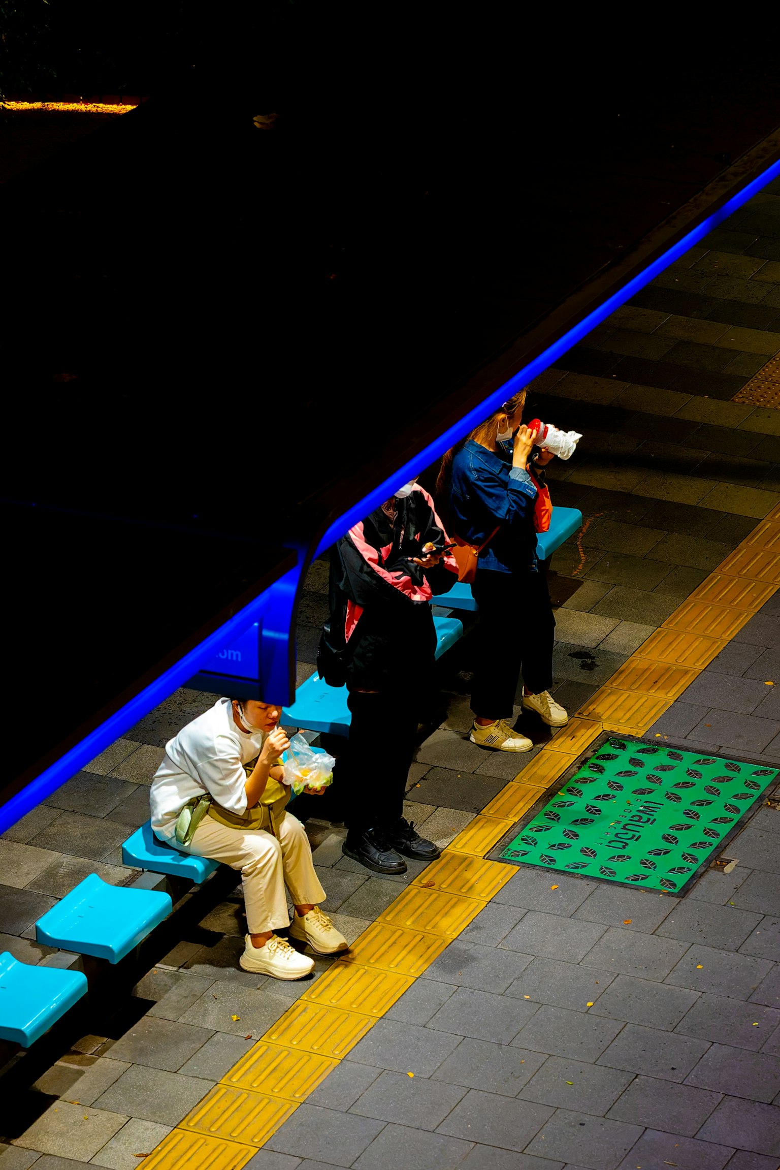 Menschen sitzen auf Bänken an einer Nachtstation mit blauer Beleuchtung