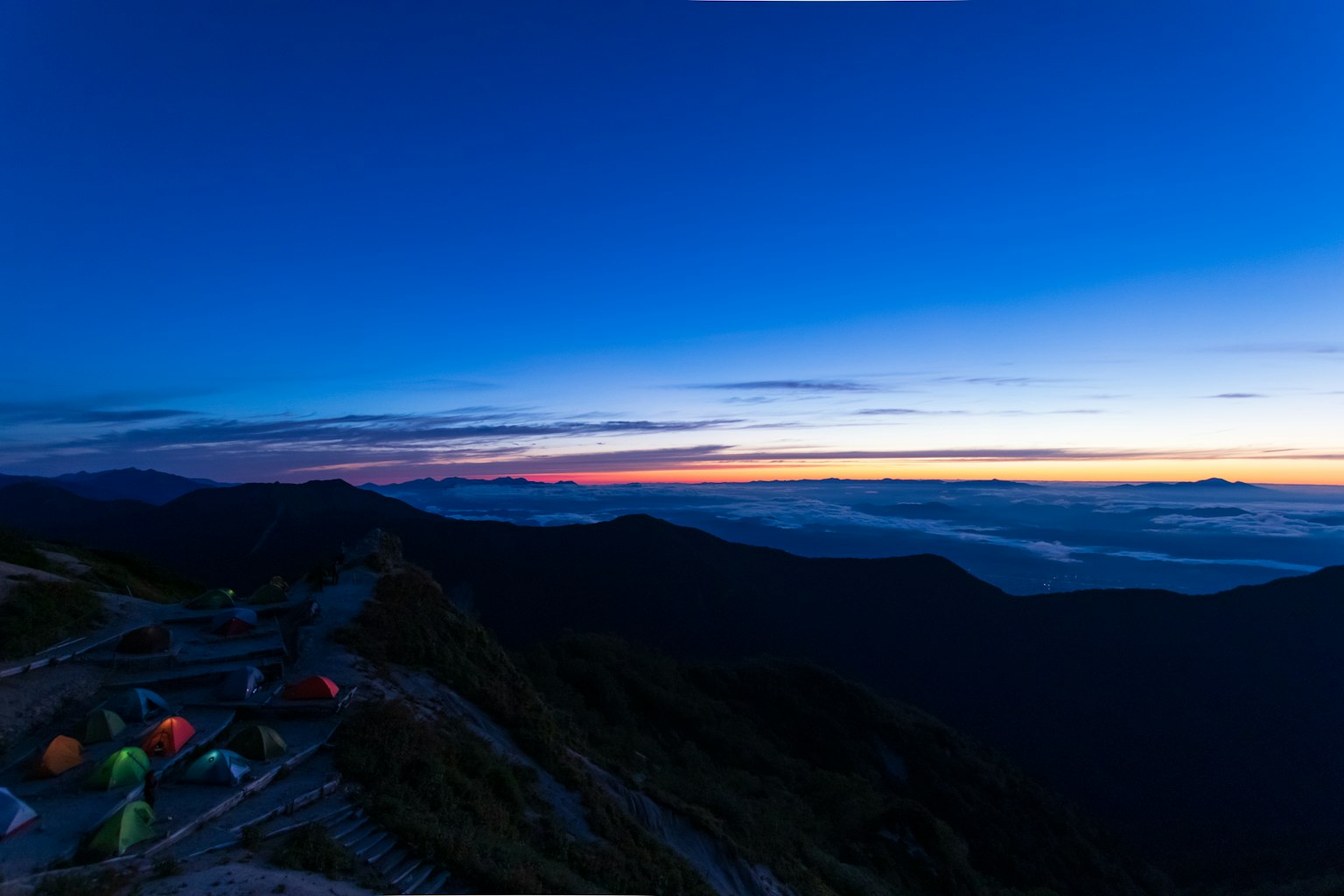 Vista panoramica delle montagne con tende colorate sotto un cielo blu