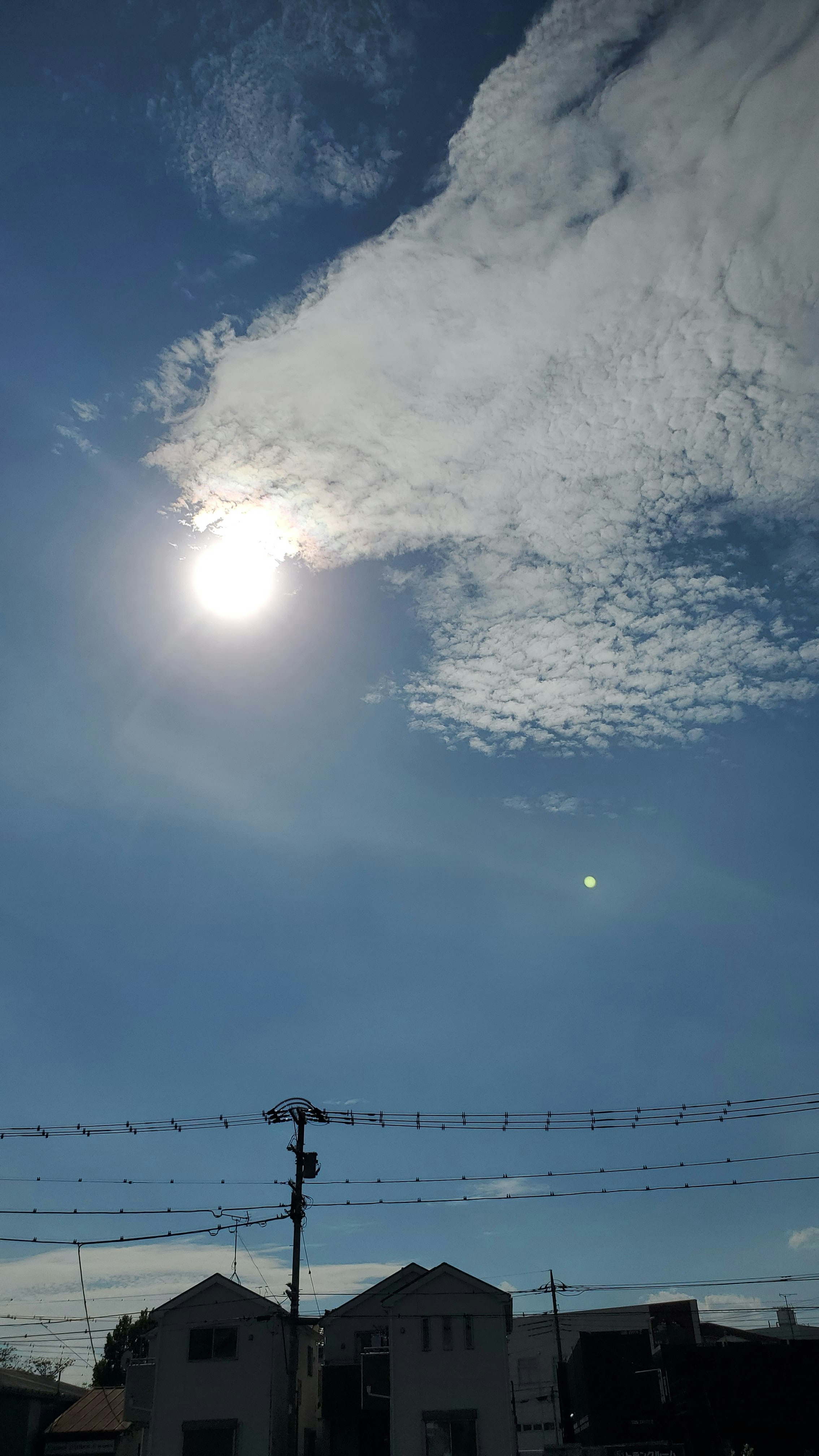 雲間から差す太陽光と青空の下の電線と家並み
