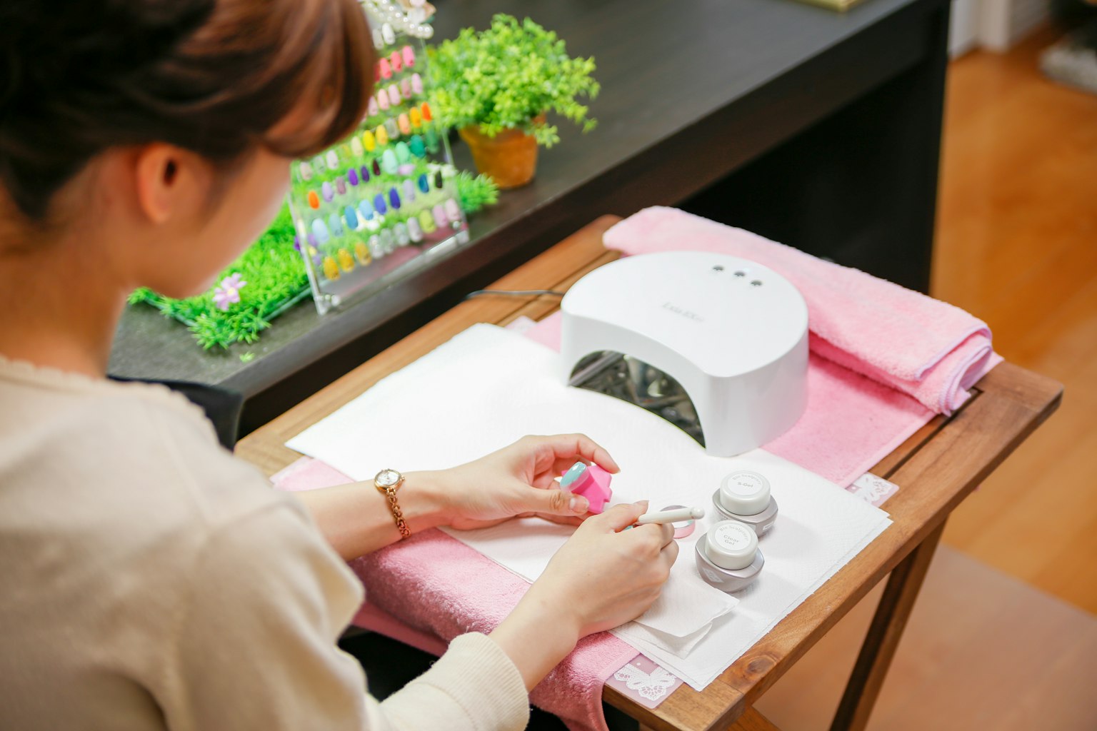 Mujer aplicando esmalte de uñas en un salón de uñas con lámpara LED y esmaltes coloridos
