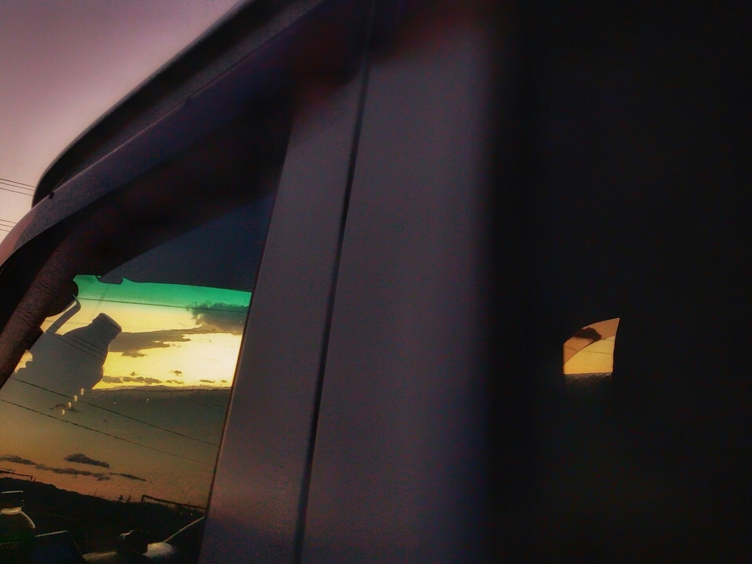 Teilansicht eines Autofensters, das einen Sonnenuntergangshimmel spiegelt