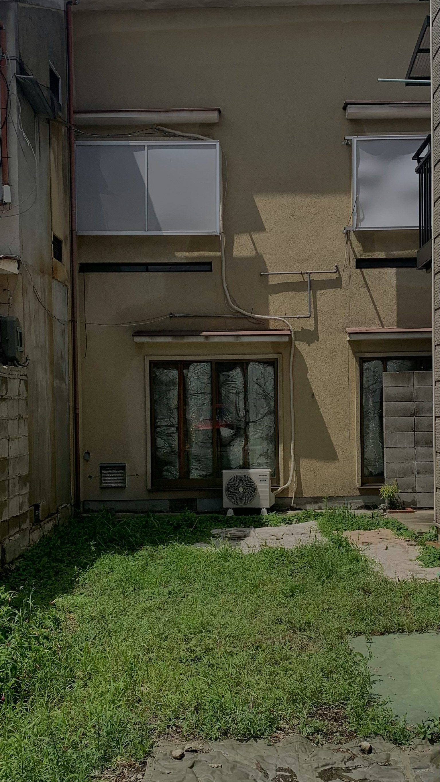 Rückansicht eines Hauses mit einem kleinen Garten, der grünes Gras und eine Klimaanlage zeigt
