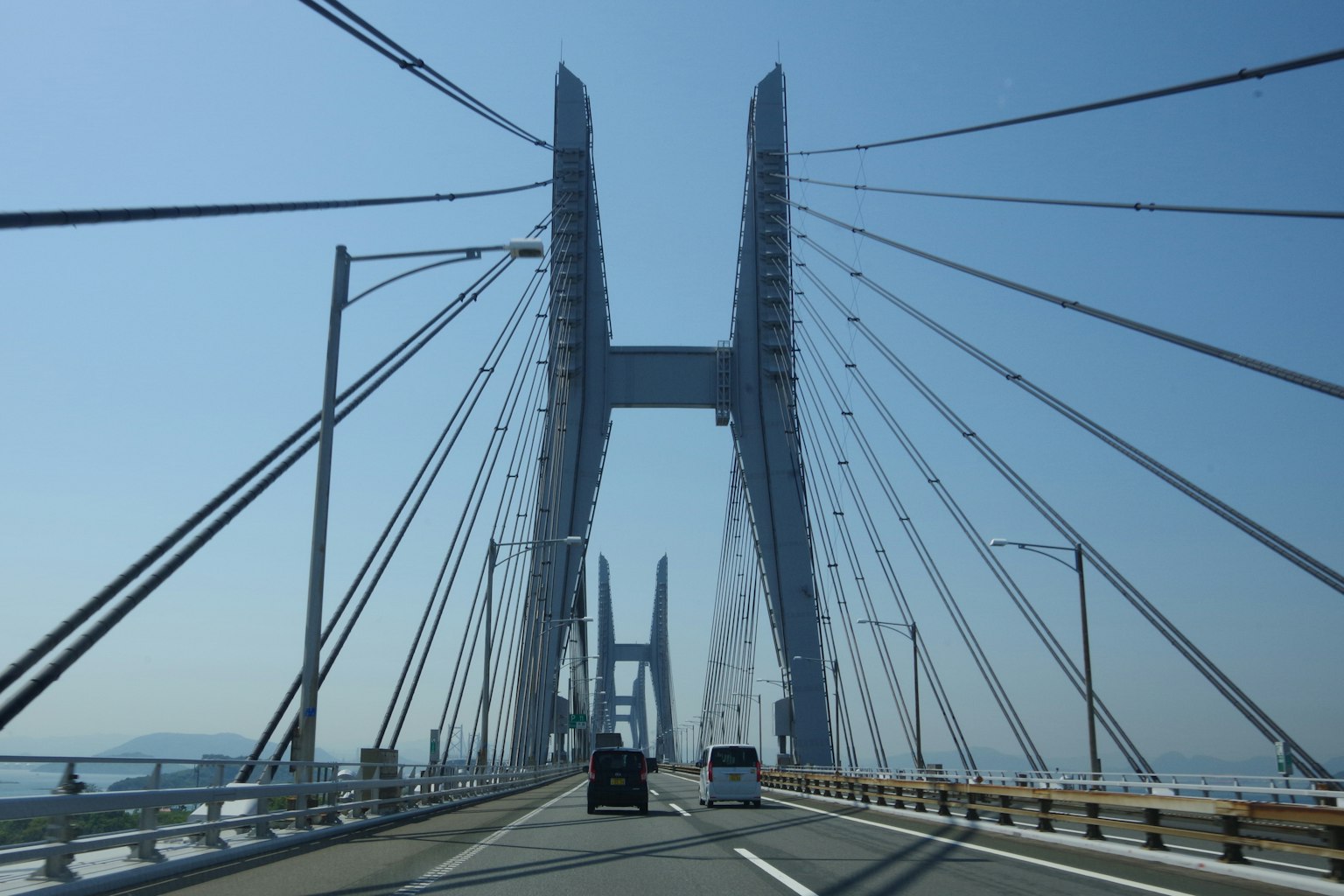 ภาพของสะพานแขวนในวันที่มีแดดออกพร้อมรถยนต์บนถนน