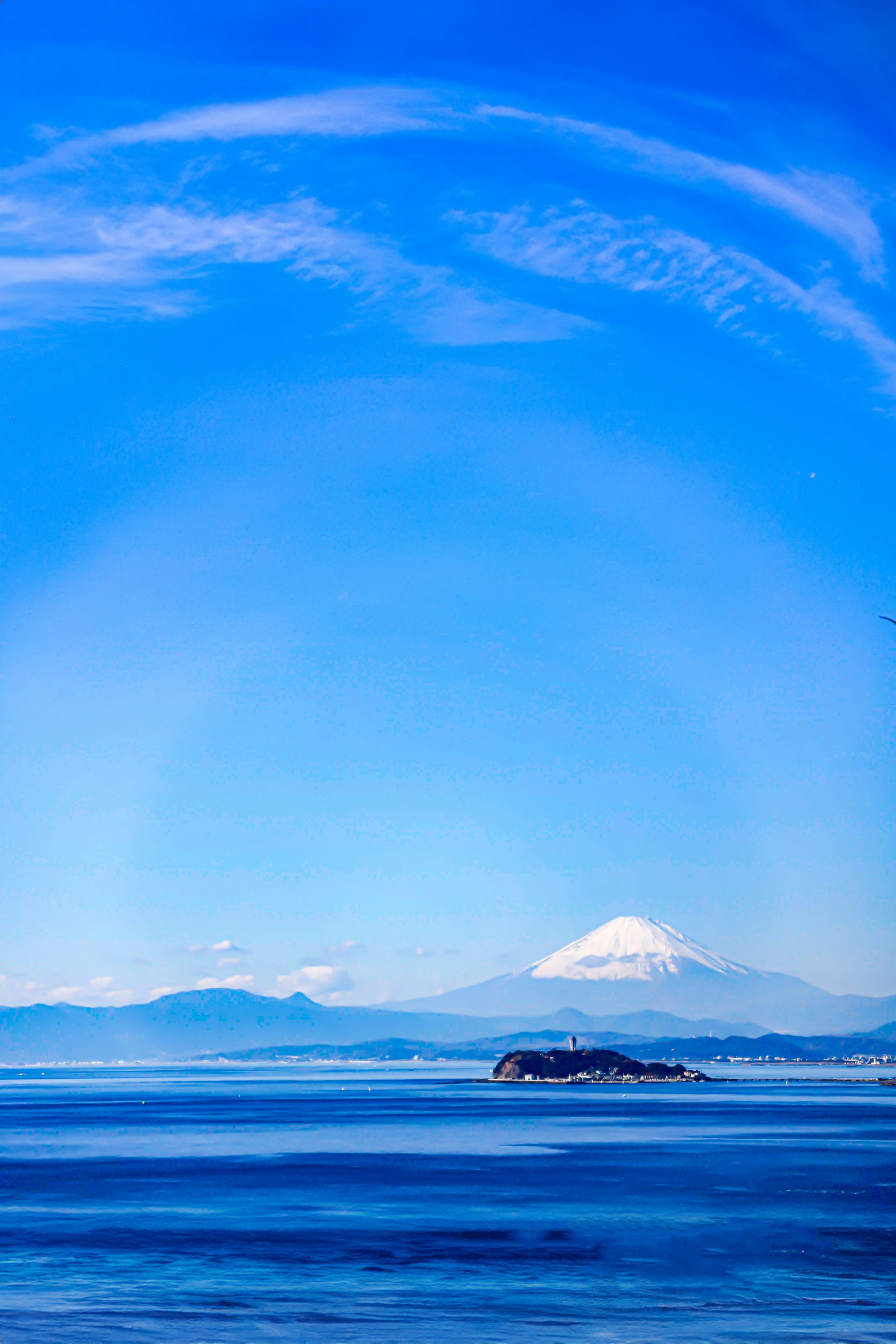 青空の下、海辺に浮かぶ島と遠くの山並み