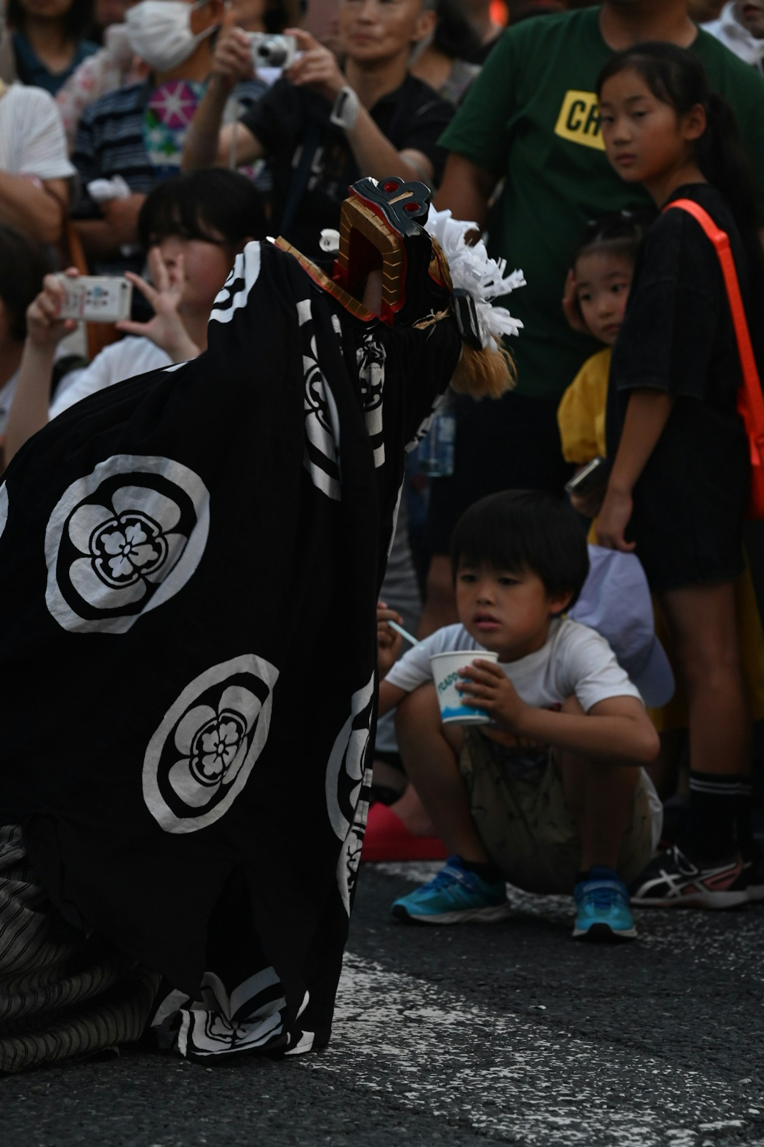 A traditional performer in a black outfit with white patterns entertaining a child sitting on the ground during a festival