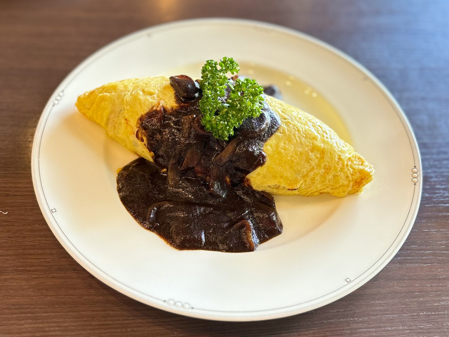 Teller mit Omelette-Reis bedeckt mit schwarzer Sauce gelbe Omelette und Petersiliengarnitur