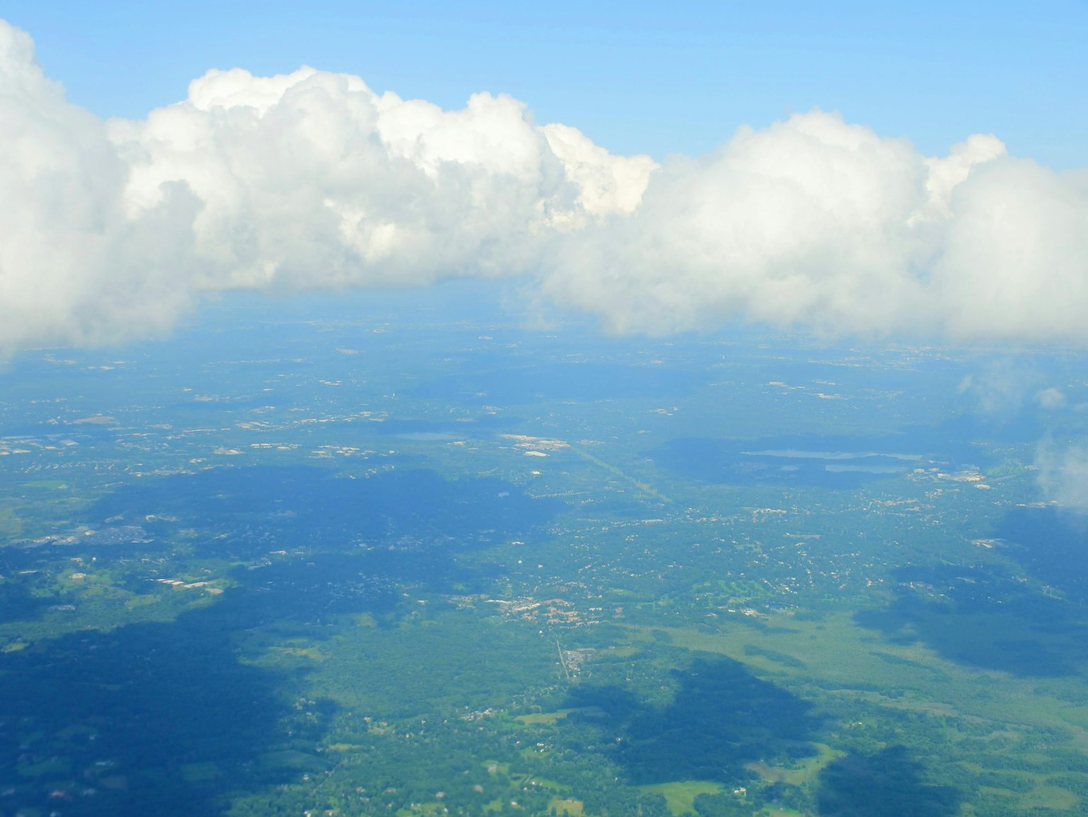 Vista aerea di paesaggi verdi sotto un cielo blu con nuvole bianche soffici