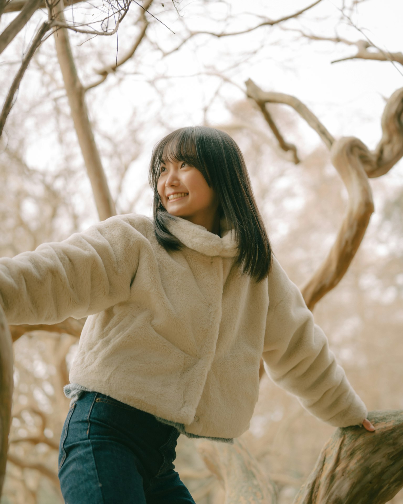 Femme souriante s'appuyant sur une branche d'arbre portant des vêtements d'hiver dans un cadre naturel