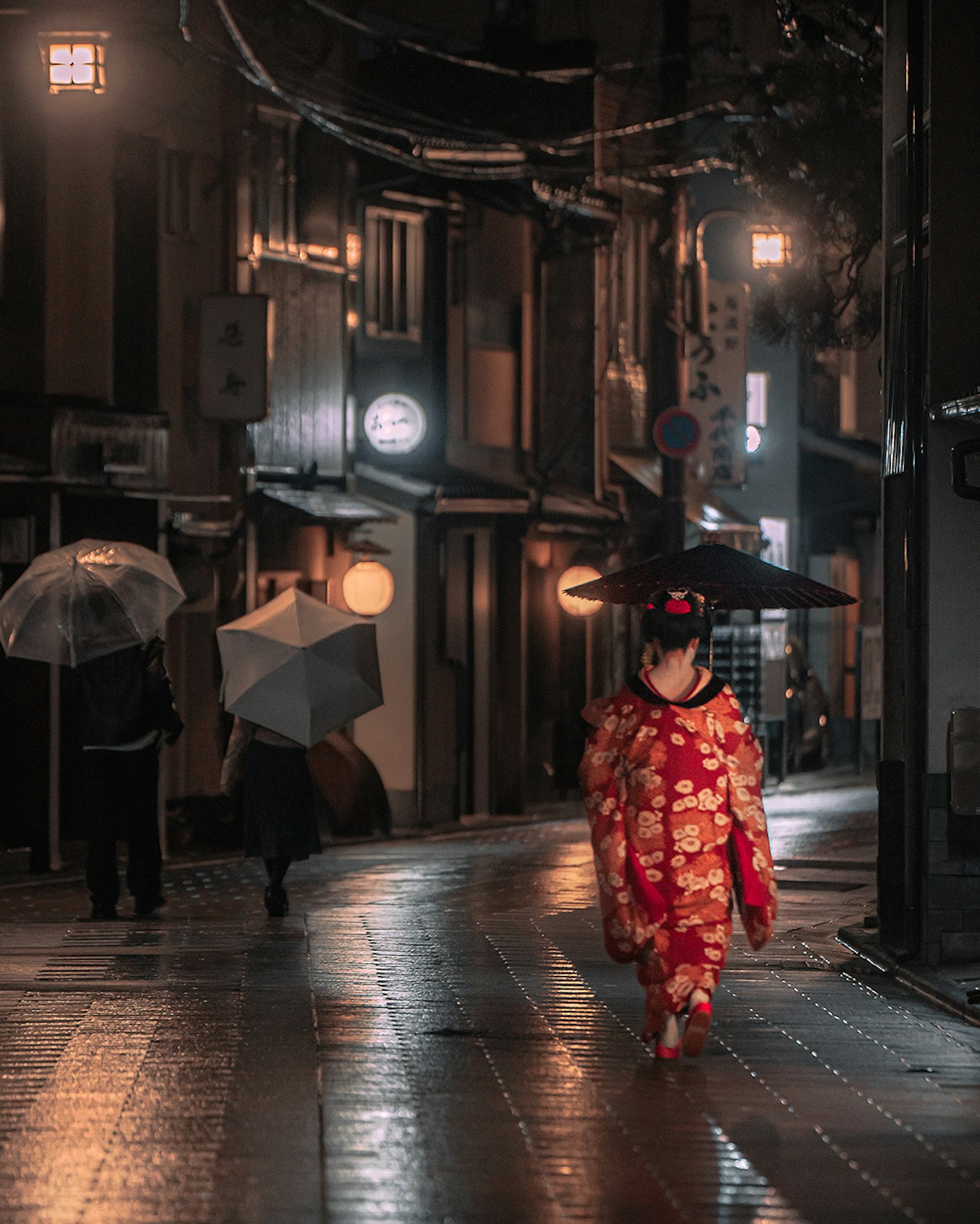 一位穿著和服的女性在雨中街道上行走，背景中有傘