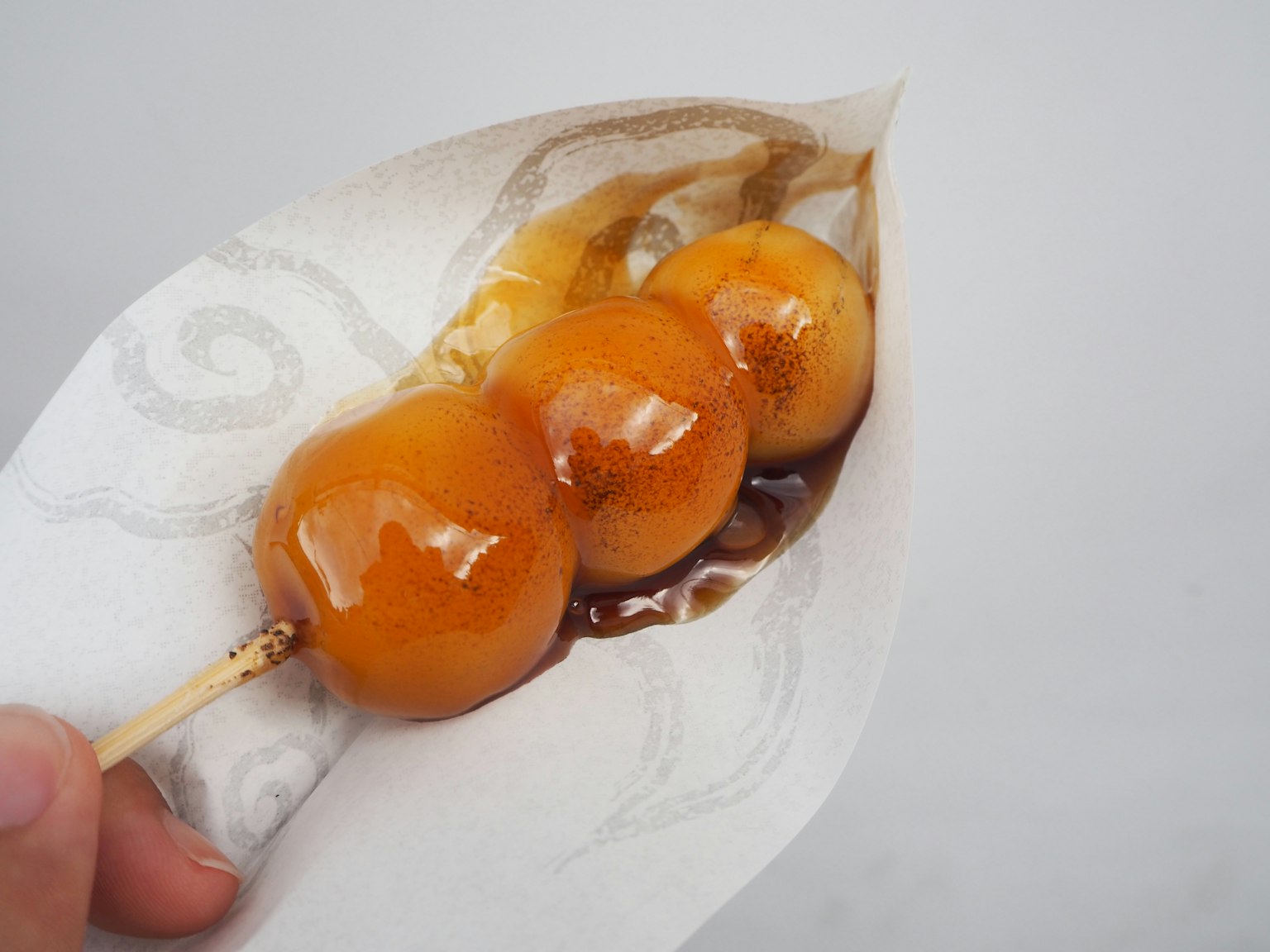 Hand, die einen Spieß mit drei Dango-Kugeln in süßer Sauce hält