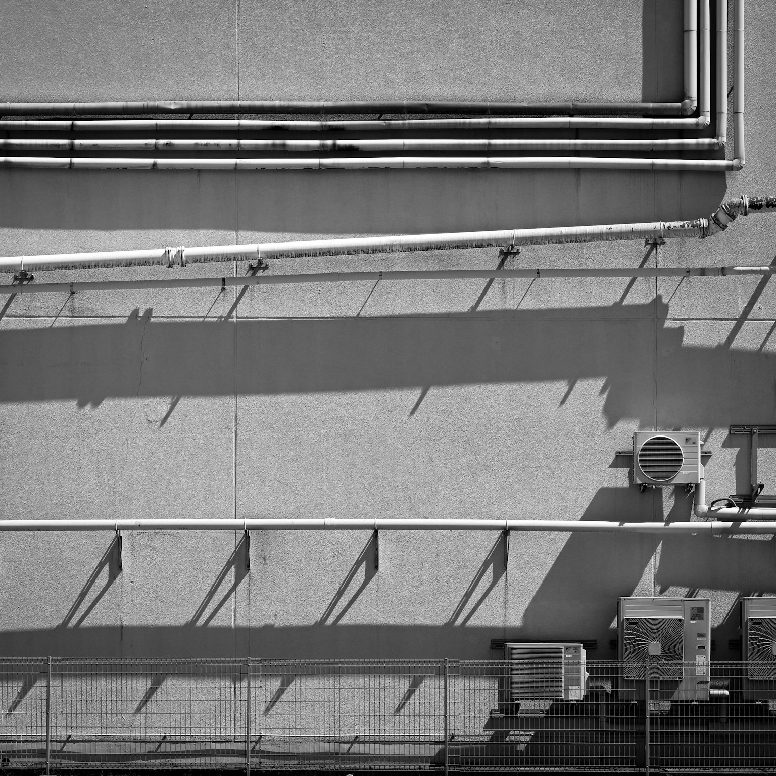 Contrasto di tubi e ombre su un muro di un edificio in bianco e nero