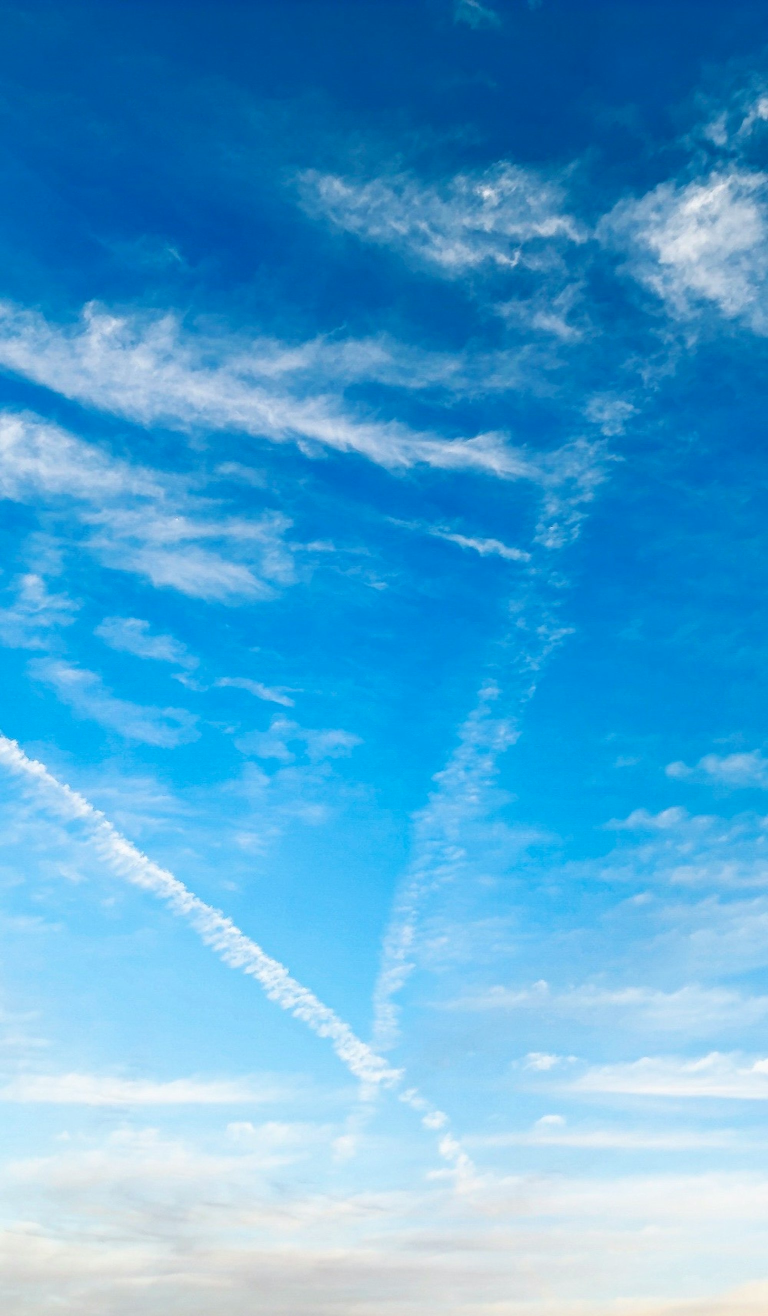 青空に広がる白い雲と飛行機雲の交差