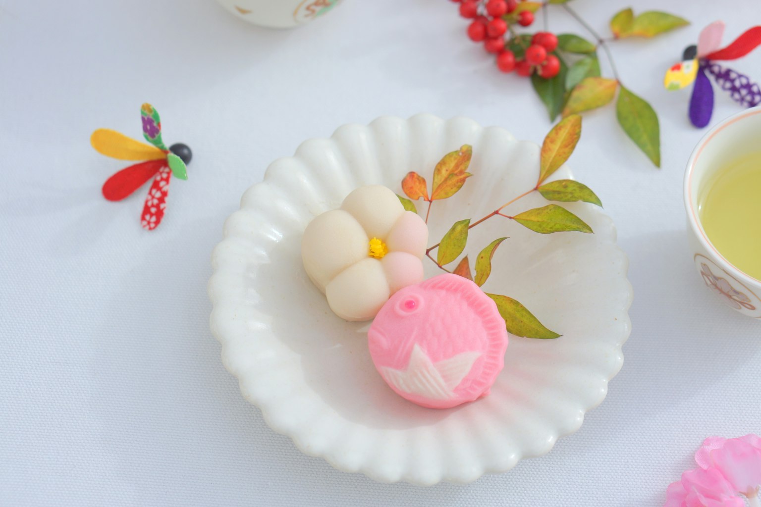 Dolci giapponesi carini su un piatto bianco con tè verde circondati da foglie decorative e bacche rosse