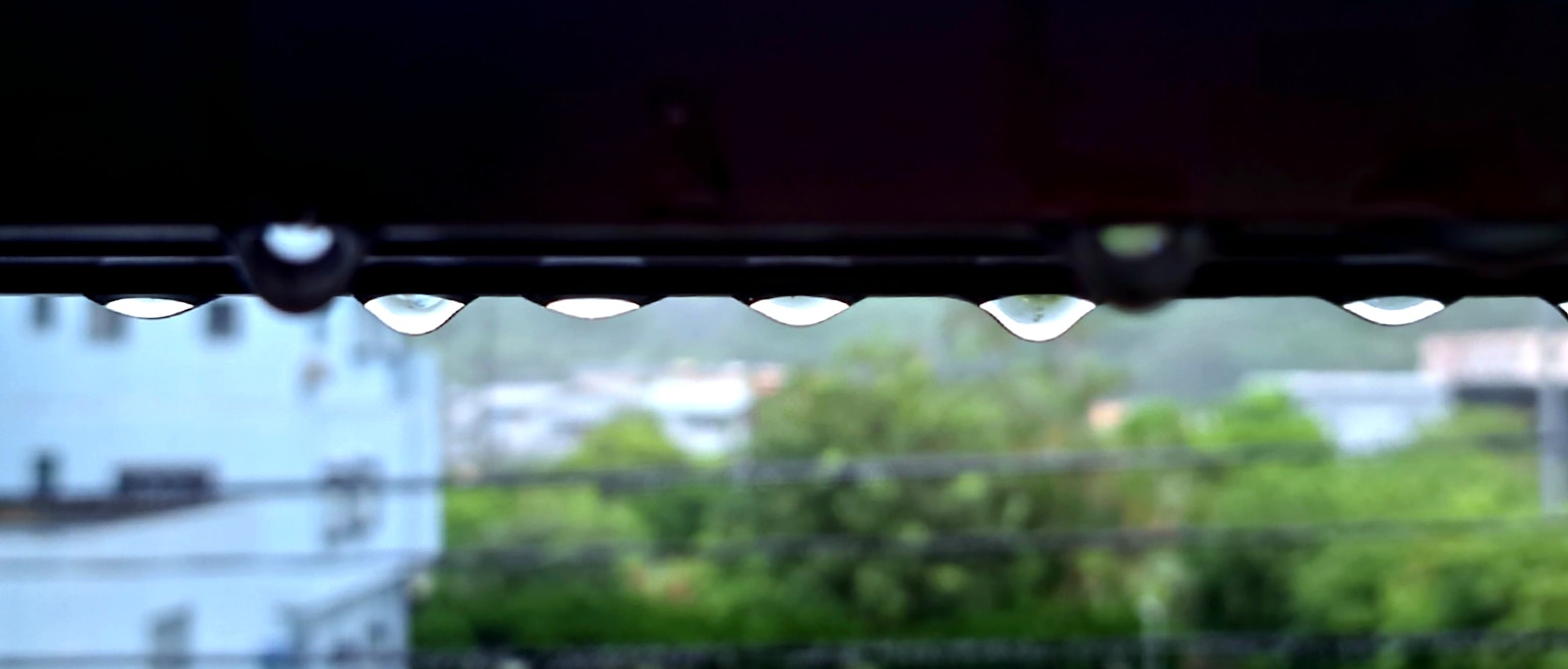 屋檐下悬挂的雨滴与模糊的绿色背景