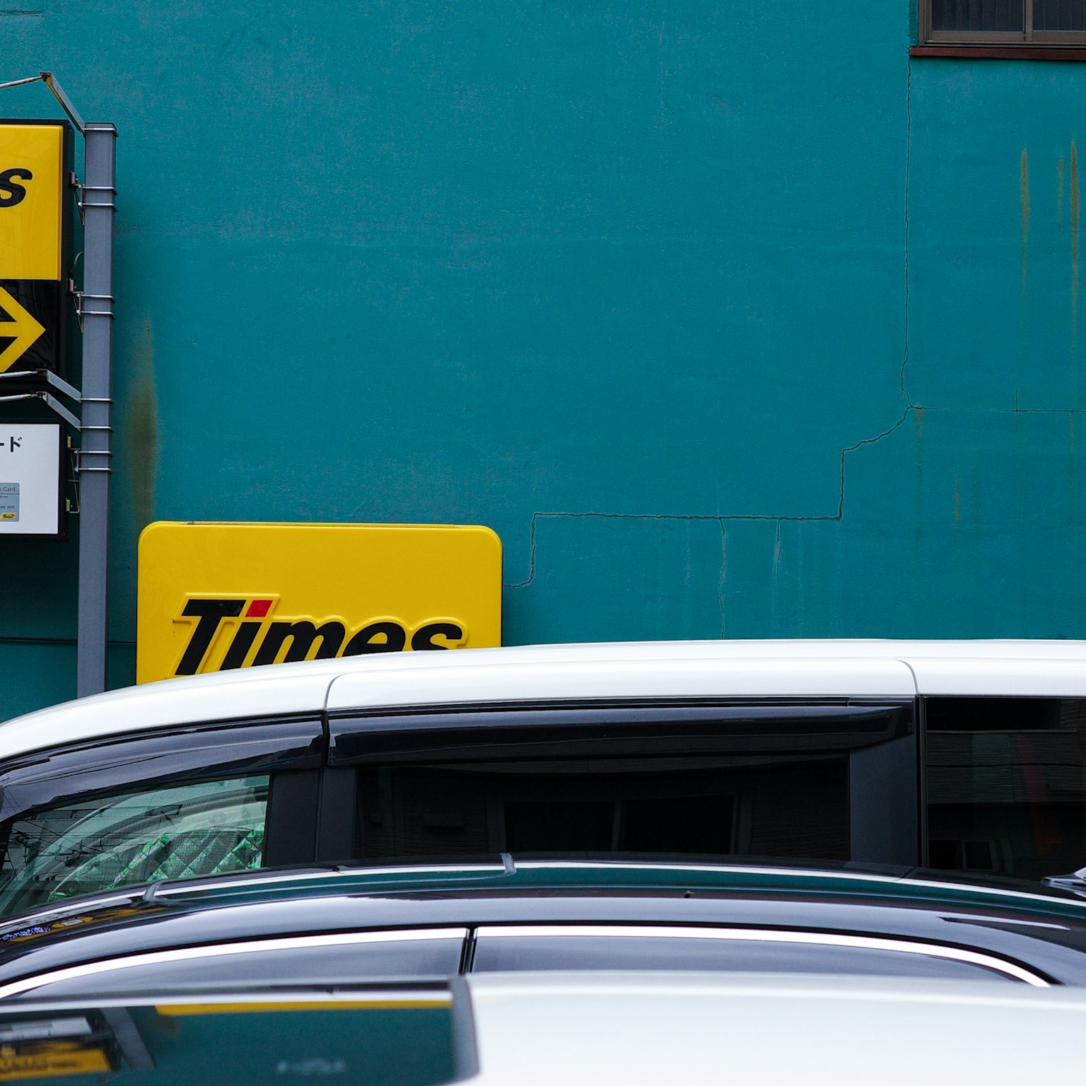 Escena con un letrero de estacionamiento y coches blancos frente a una pared azul