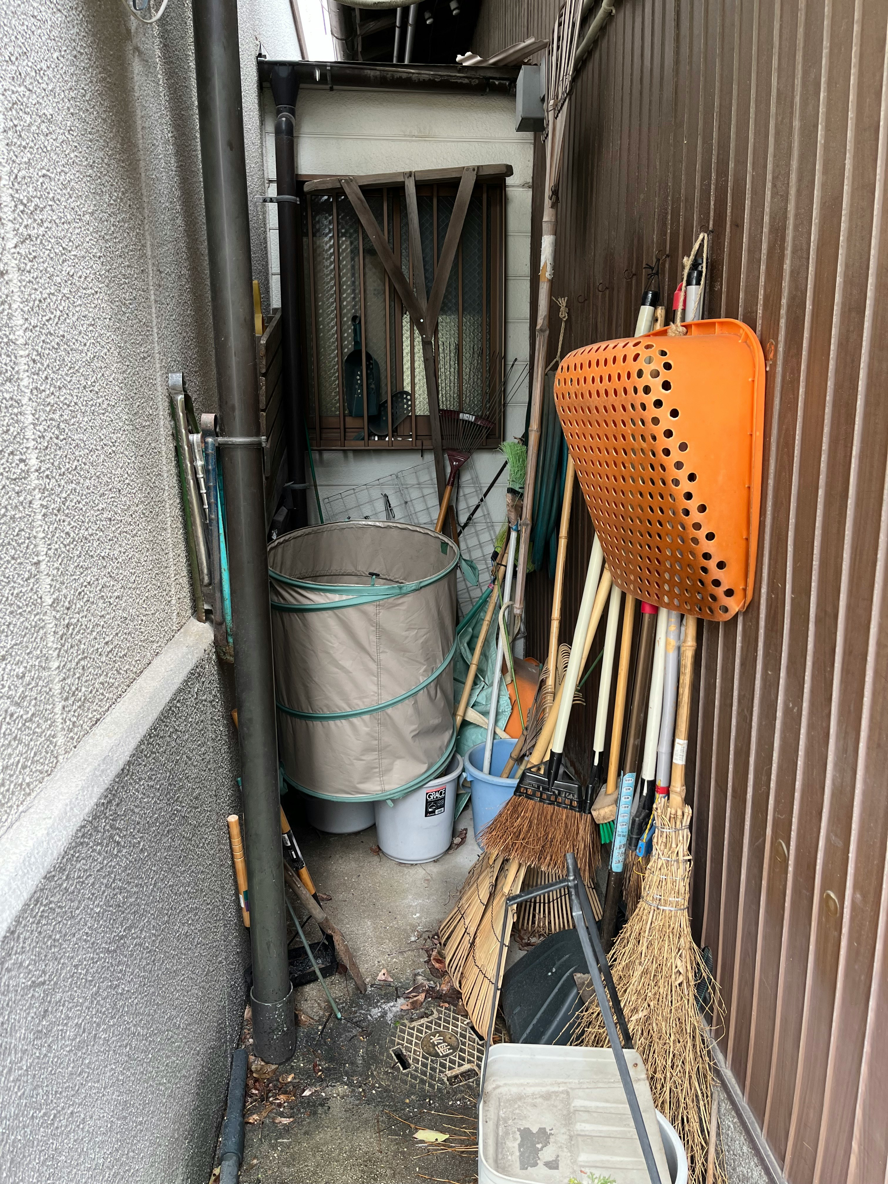 狭い路地の物置スペースに並ぶ清掃用具とバケツ