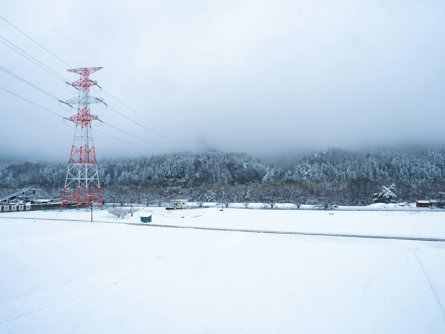 Paisaje nevado con líneas eléctricas rojas y montañas al fondo