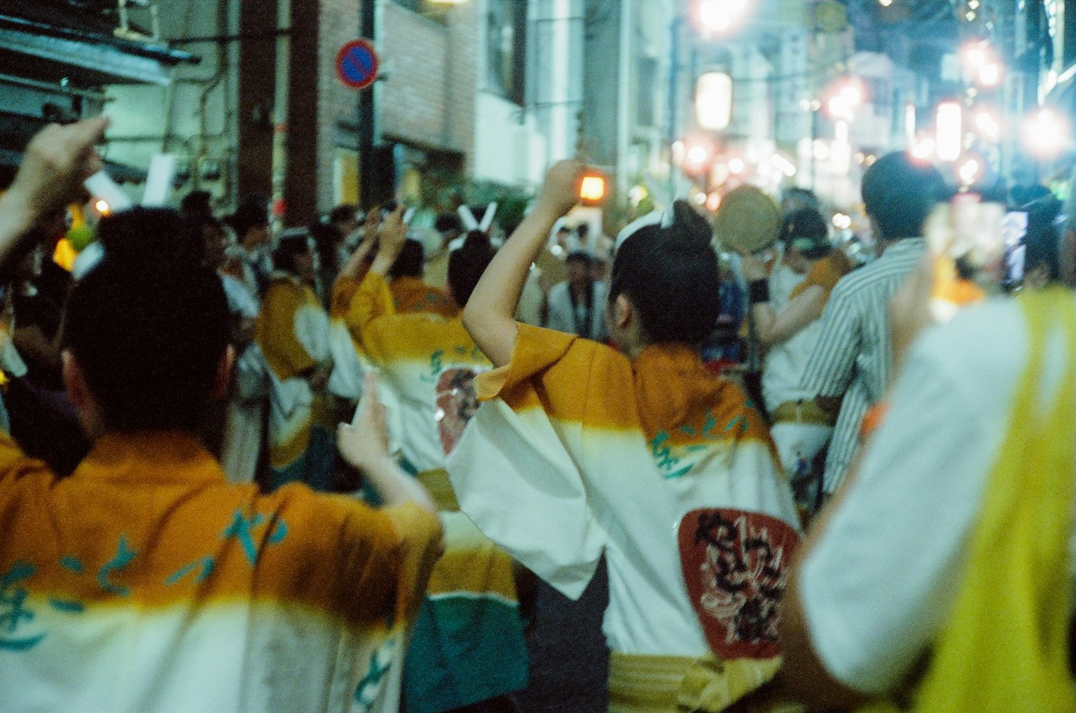 Crowd of people dancing in traditional attire during a festival in a vibrant night street