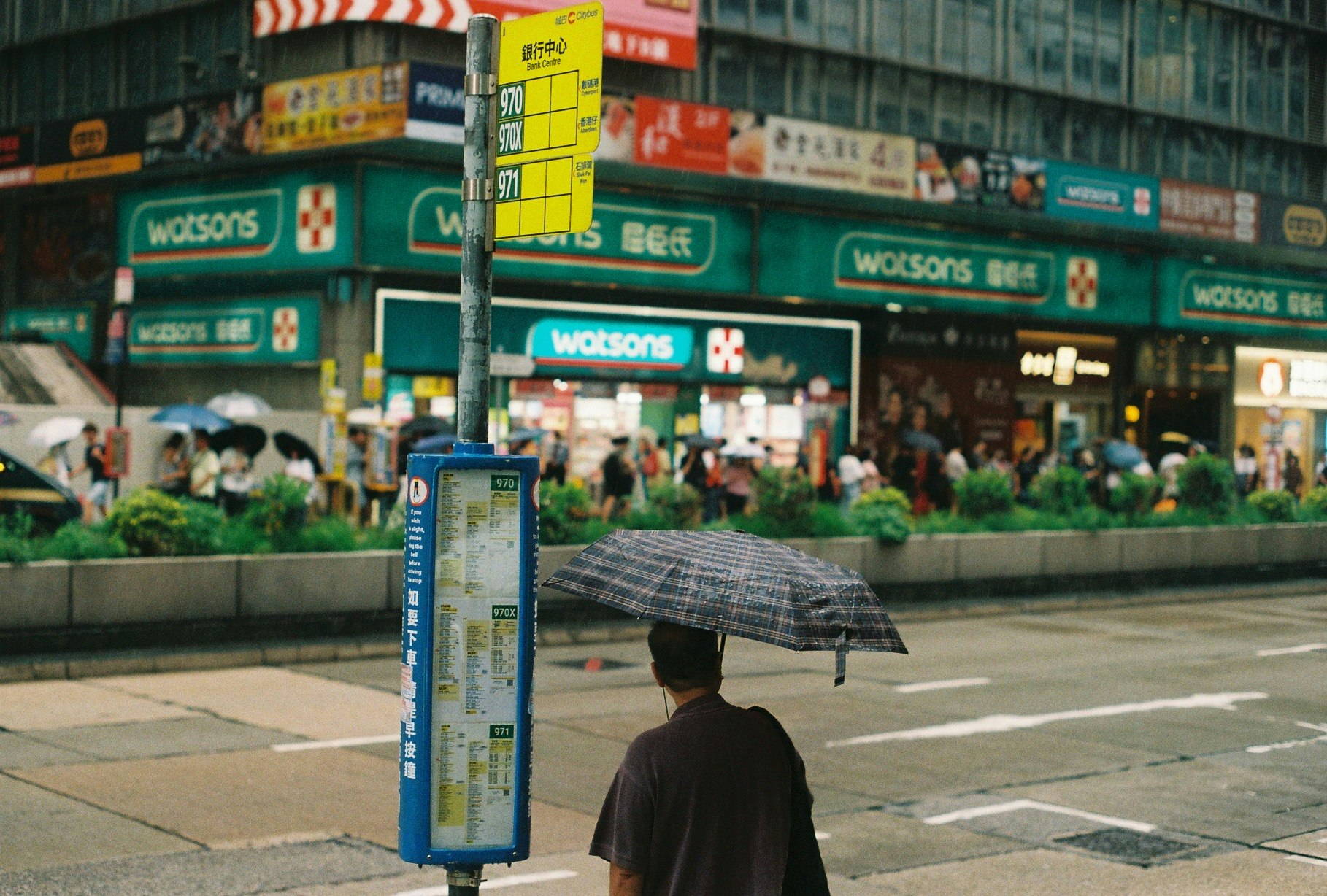 雨の中の傘をさす人とバス停の看板がある街角