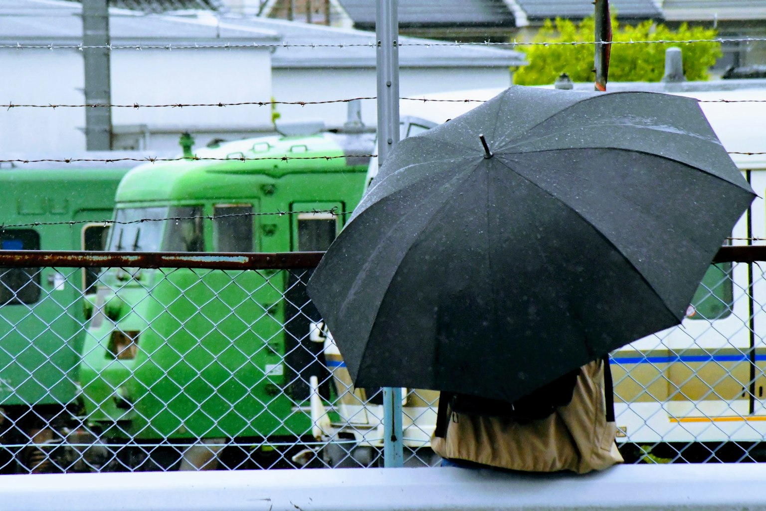 Une personne tenant un parapluie noir avec un train vert en arrière-plan