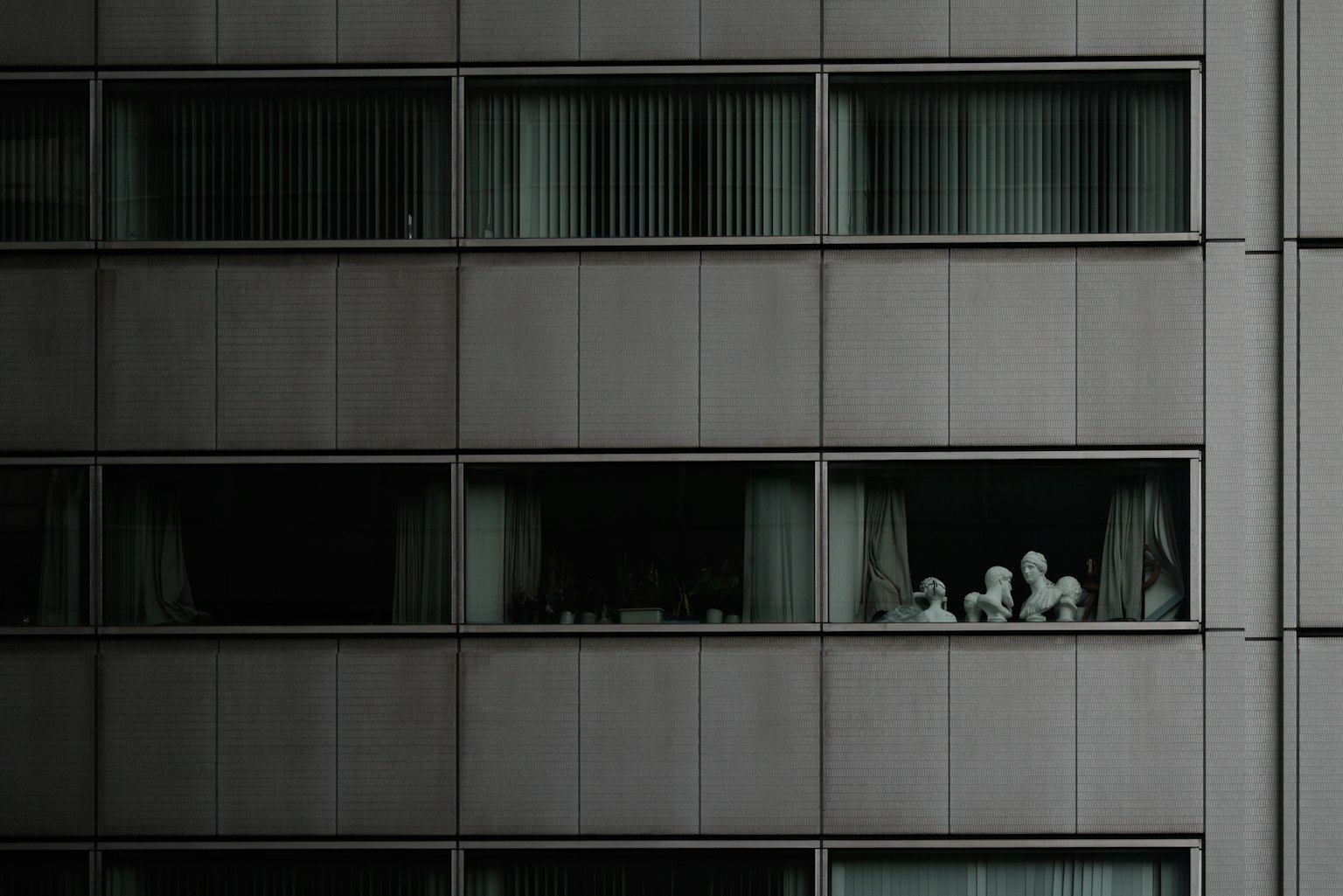White sculptures resembling figures in windows of a gray building