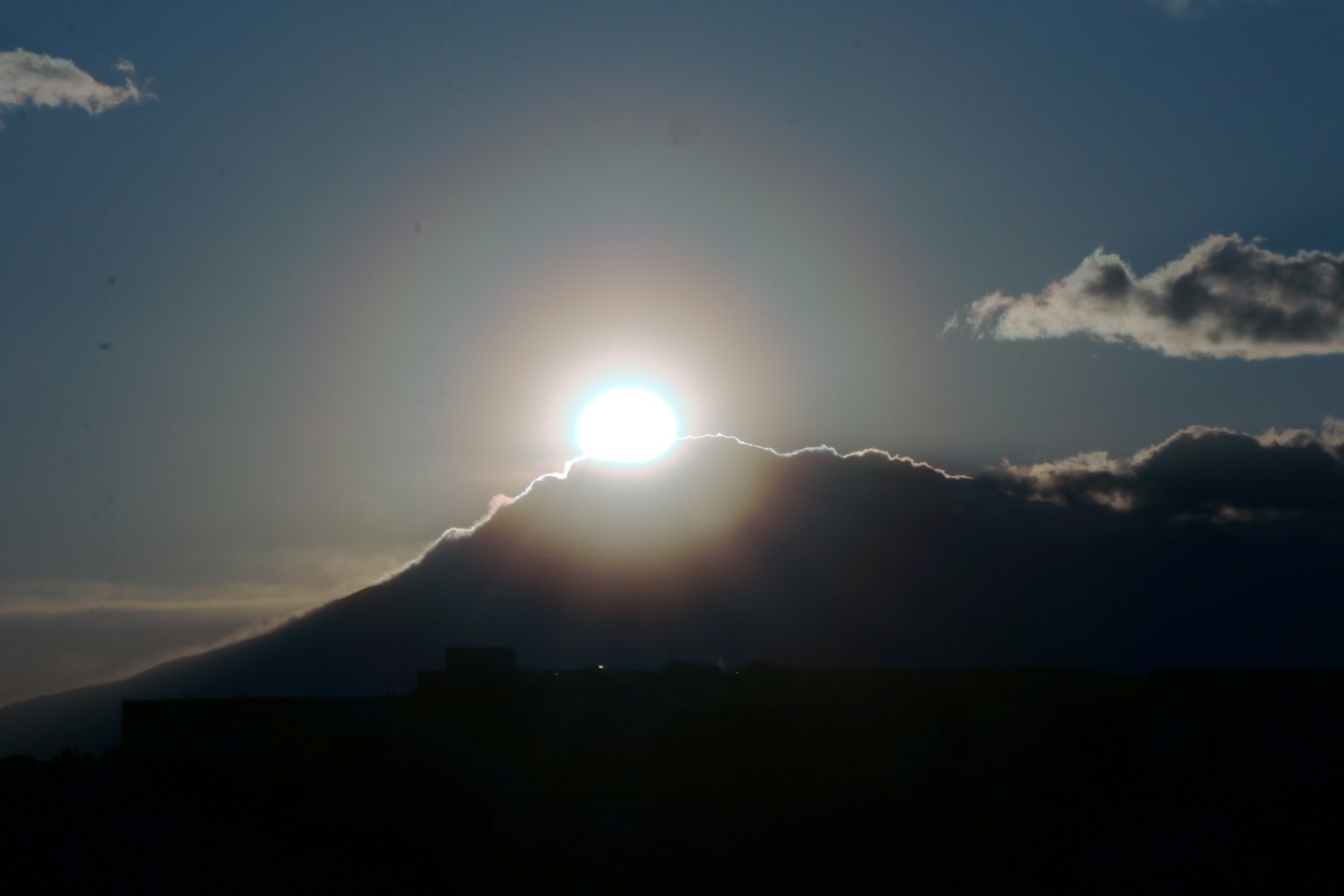 Sol saliendo sobre una montaña con nubes en silueta