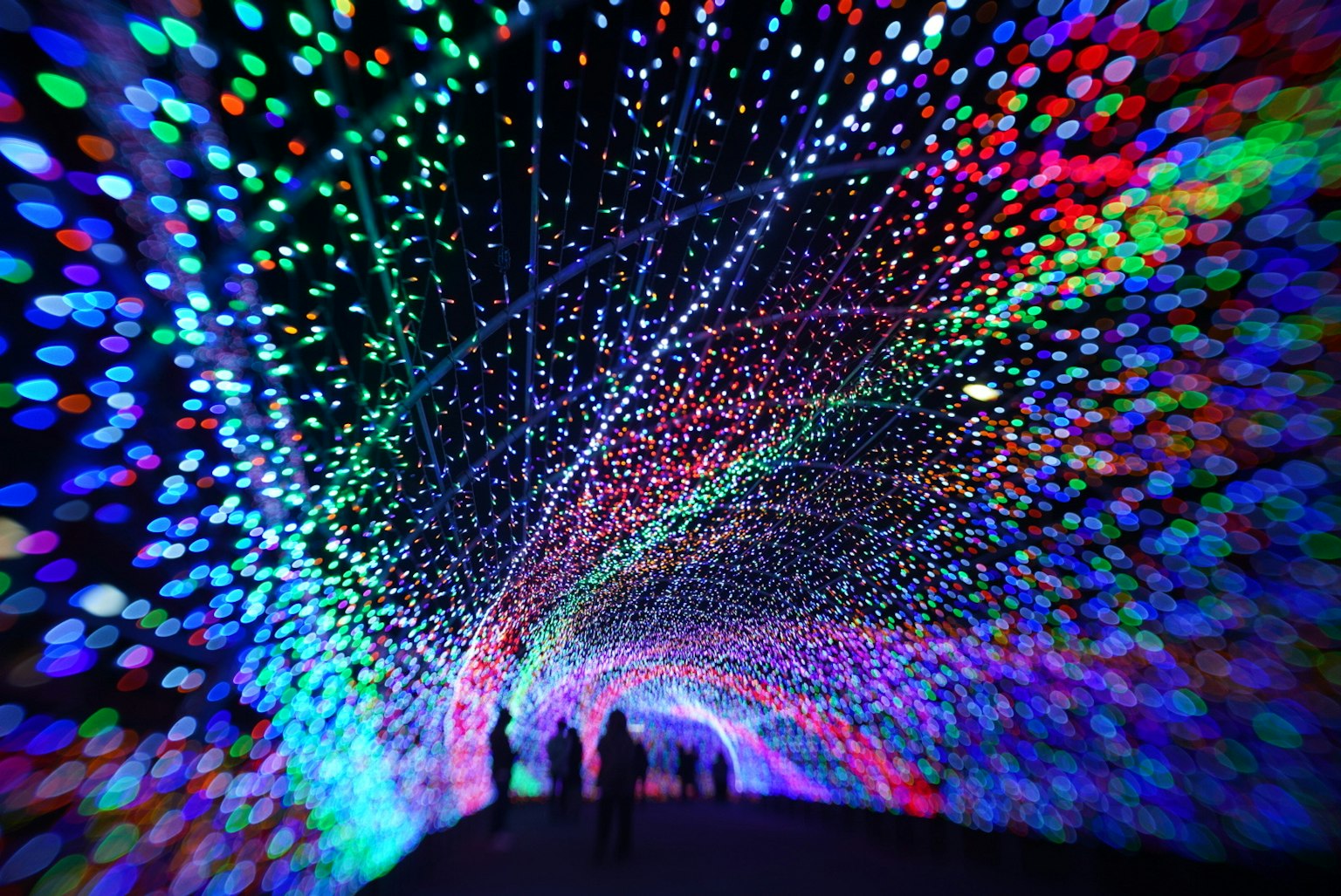 Luci colorate creano un effetto tunnel con silhouette di persone che camminano attraverso